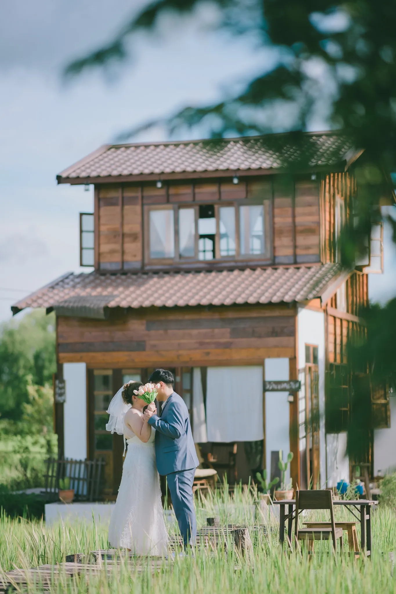 A couple kissing on the lawn in front of a two-story wooden house
