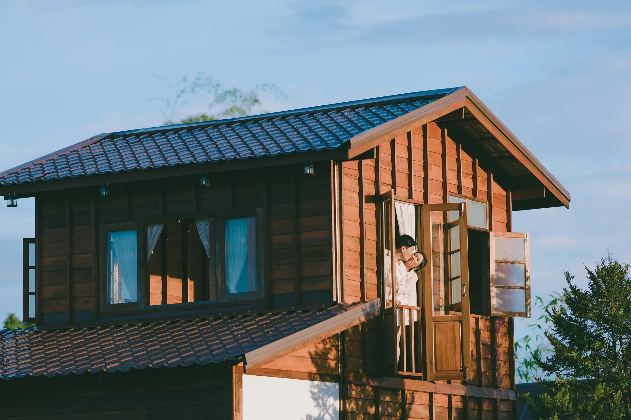 A couple looking out from the upstairs window of a wooden house in golden light
