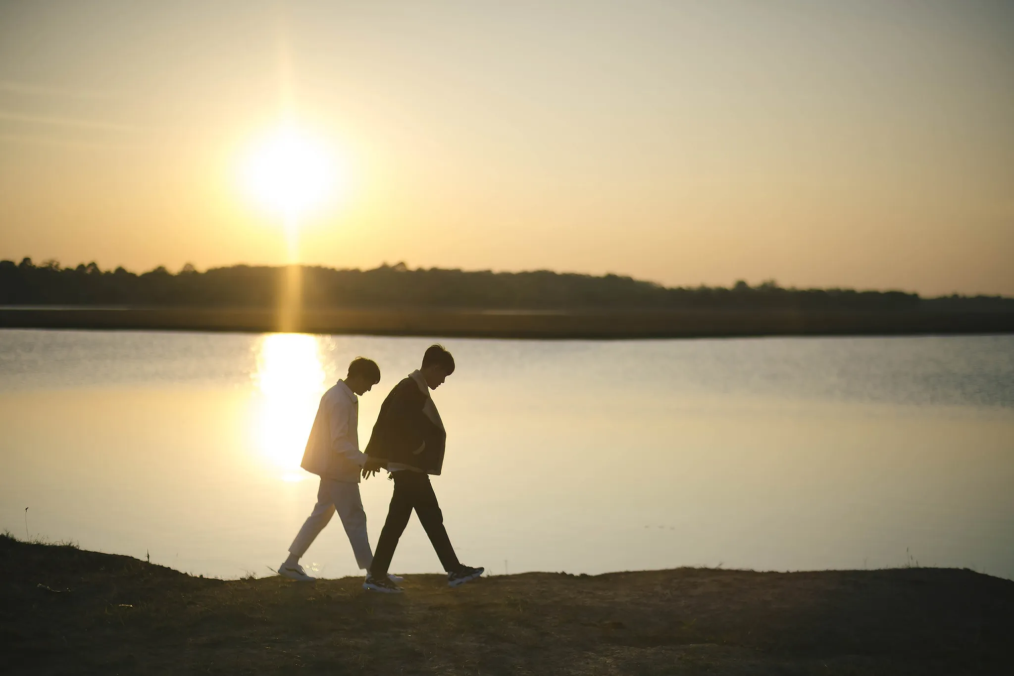 Two people silhouetted walking along a lakeshore toward the setting sun