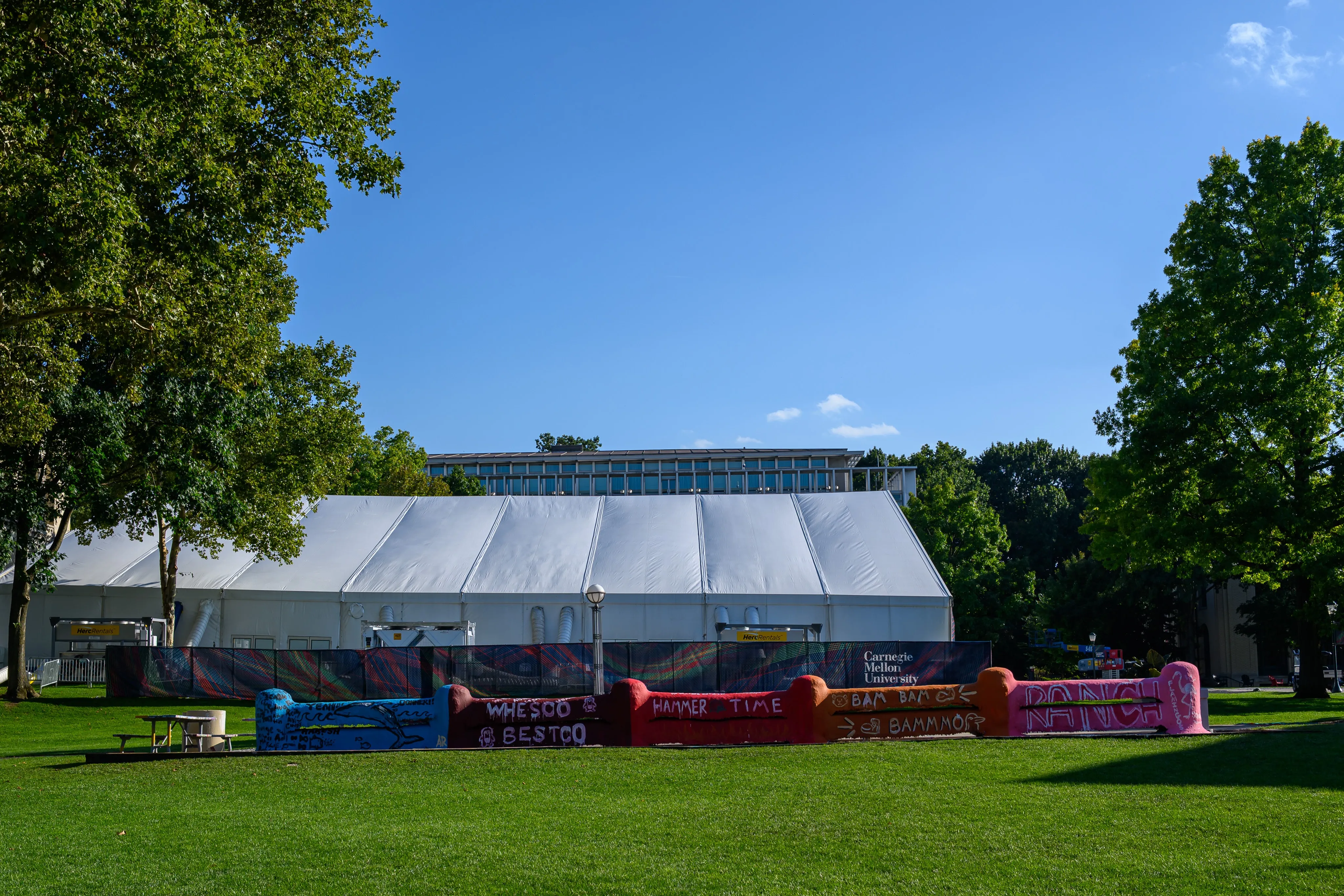 A large white event tent set up on a campus lawn between trees.