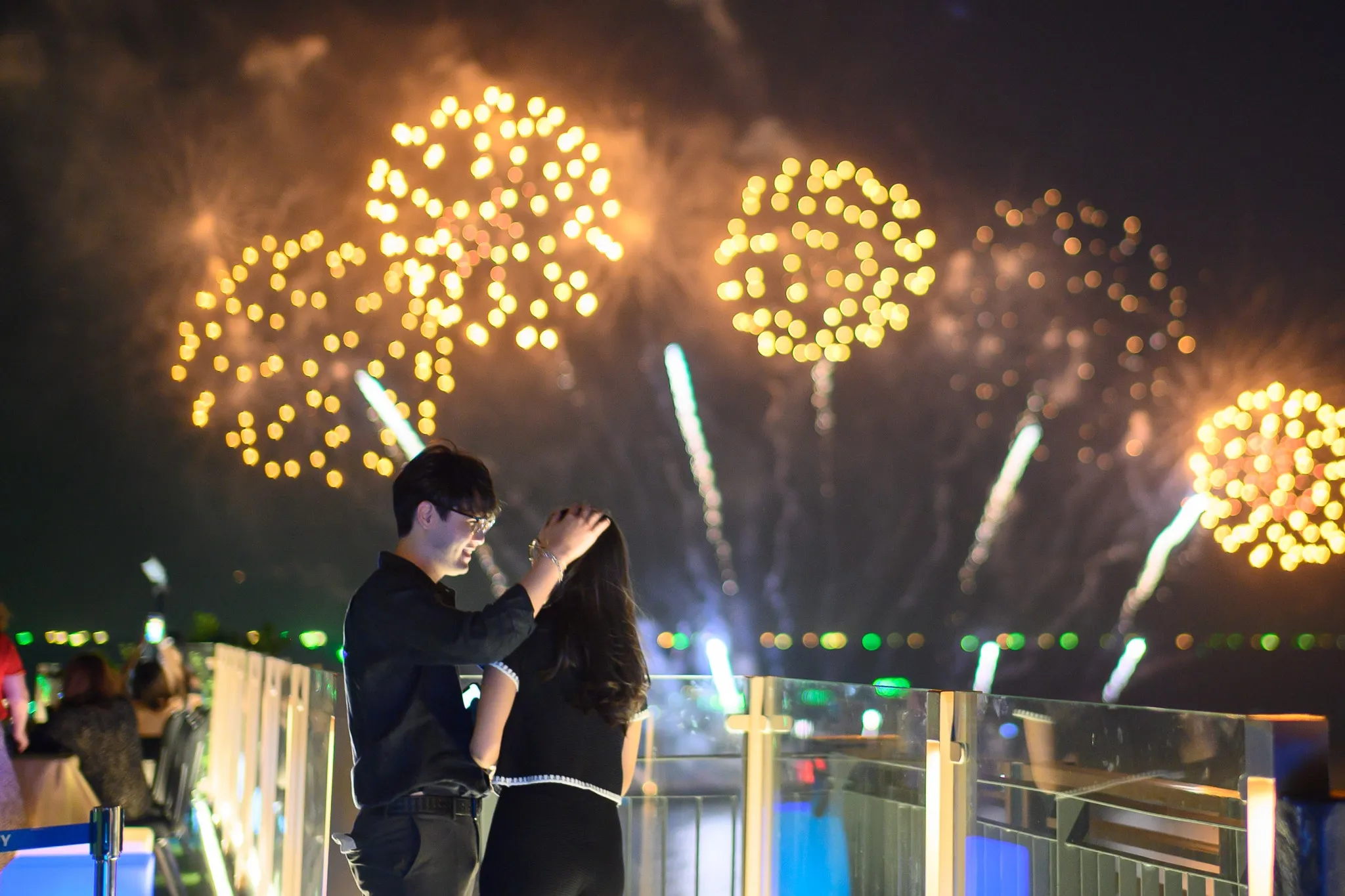 A couple embracing on a rooftop terrace beneath golden fireworks