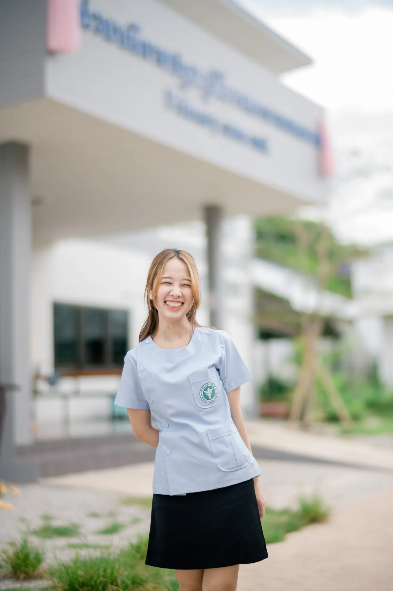 A laughing woman in a light blue health-worker uniform standing outside a clinic building