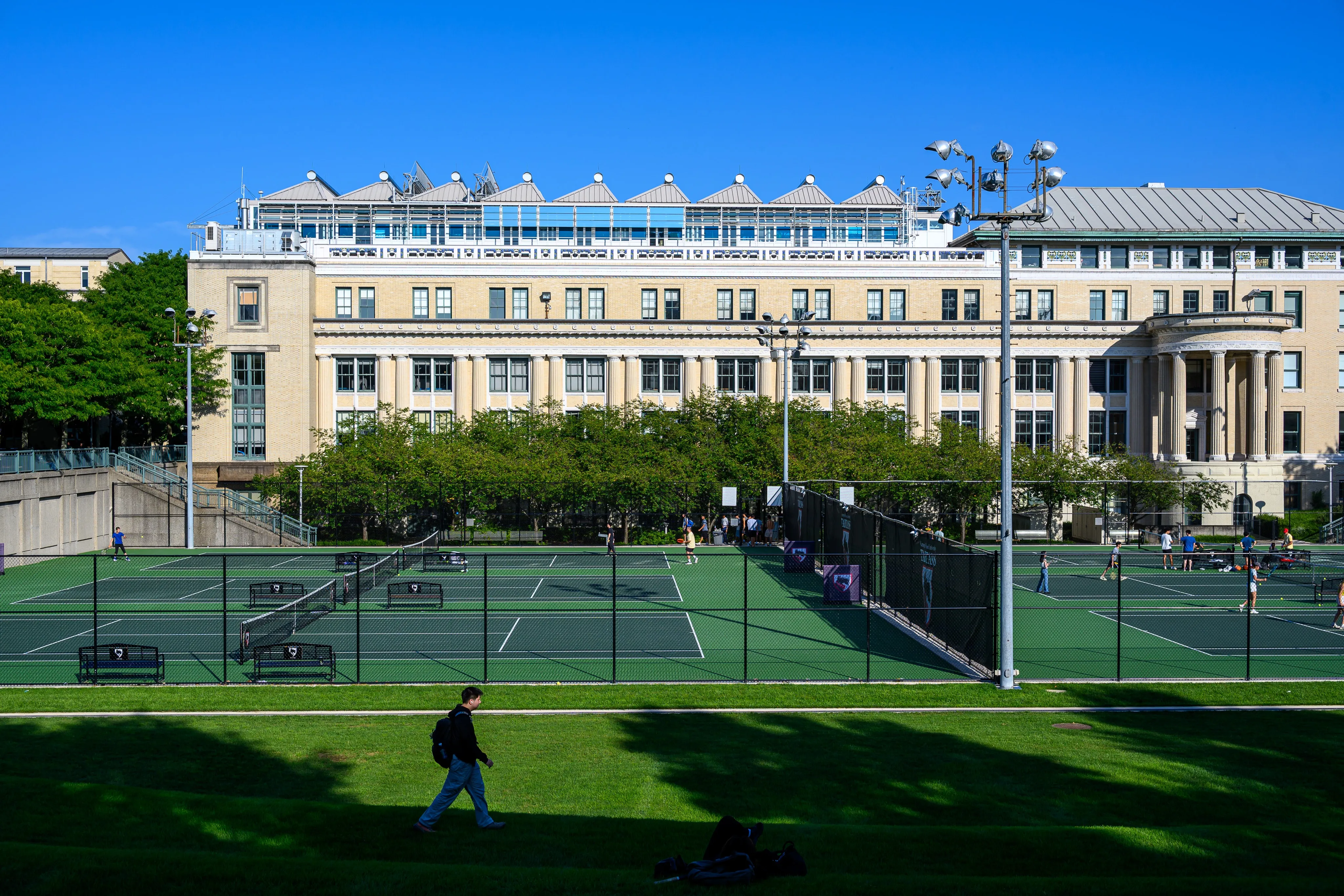A domed academic building overlooking empty tennis courts on a bright afternoon.