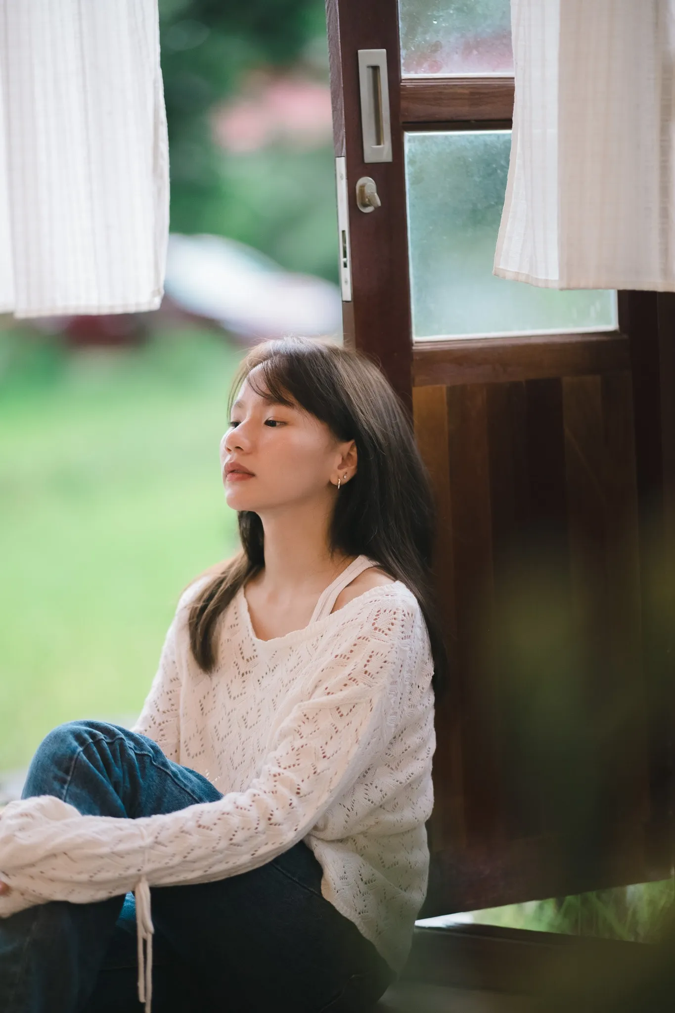 A woman in a white knit sweater sitting in an open wooden doorway with her eyes closed