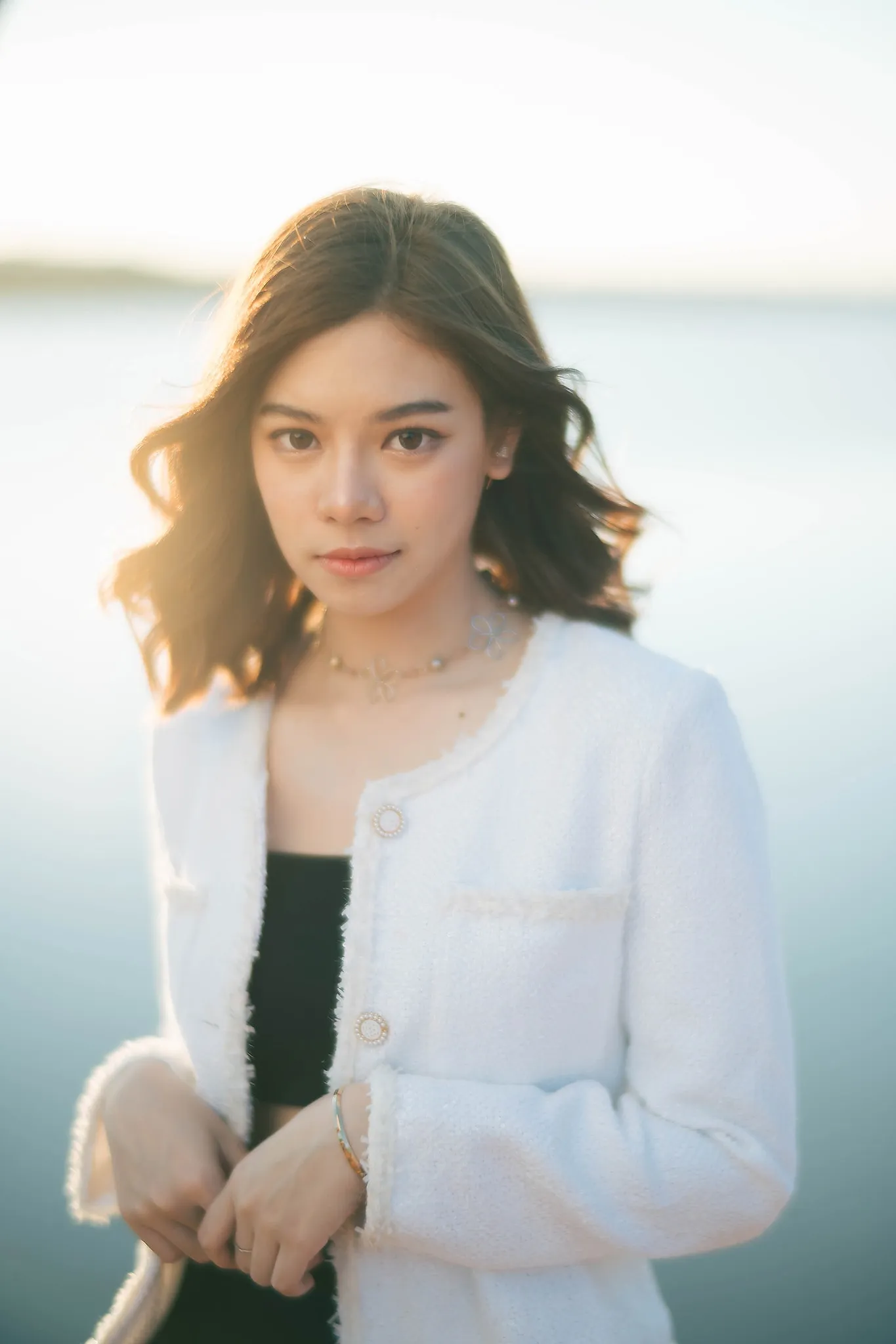 A woman with wavy hair in a white tweed jacket in soft light beside the water