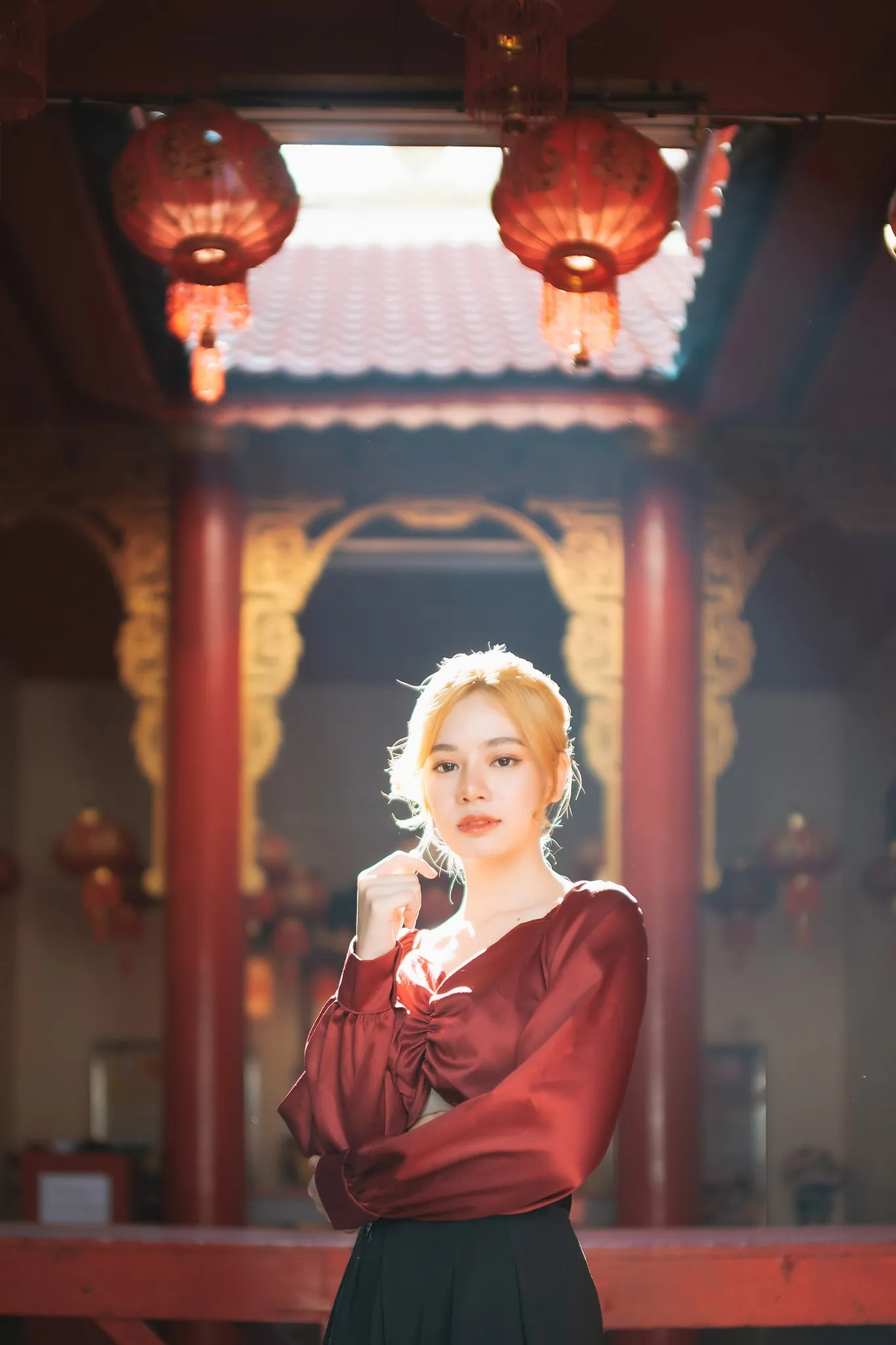 A woman in a red satin blouse posing beneath red lanterns in a Chinese shrine