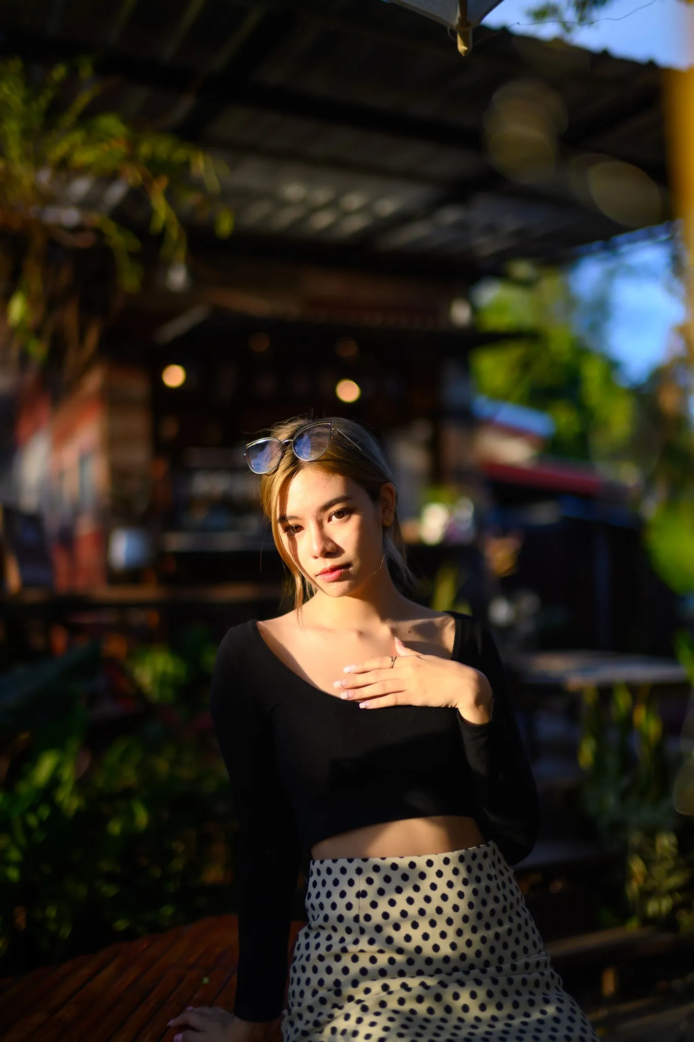 A woman in a black top and polka-dot skirt with sunglasses in her hair, touching her collarbone