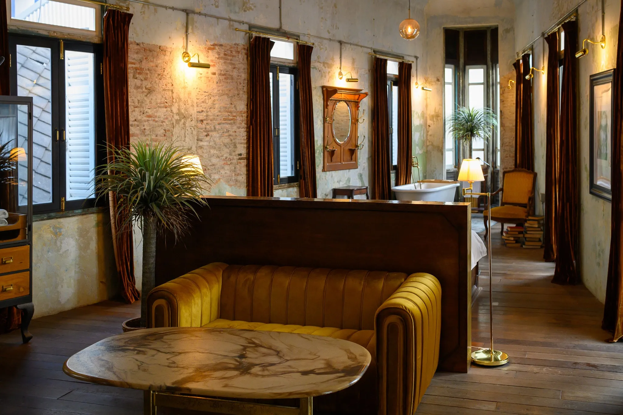 A hotel suite with a mustard velvet sofa, marble table, and weathered plaster walls