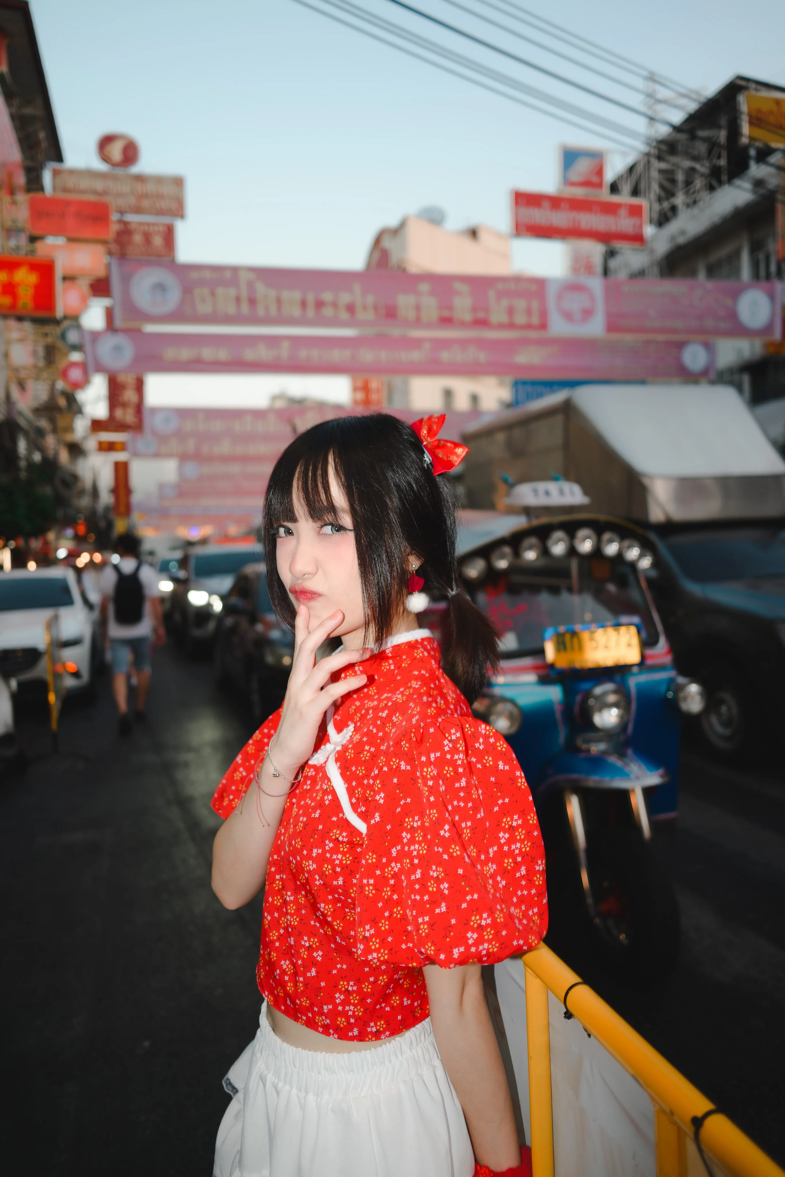A woman in a red floral top posing on a busy Chinatown street with a tuk-tuk and red banners behind her