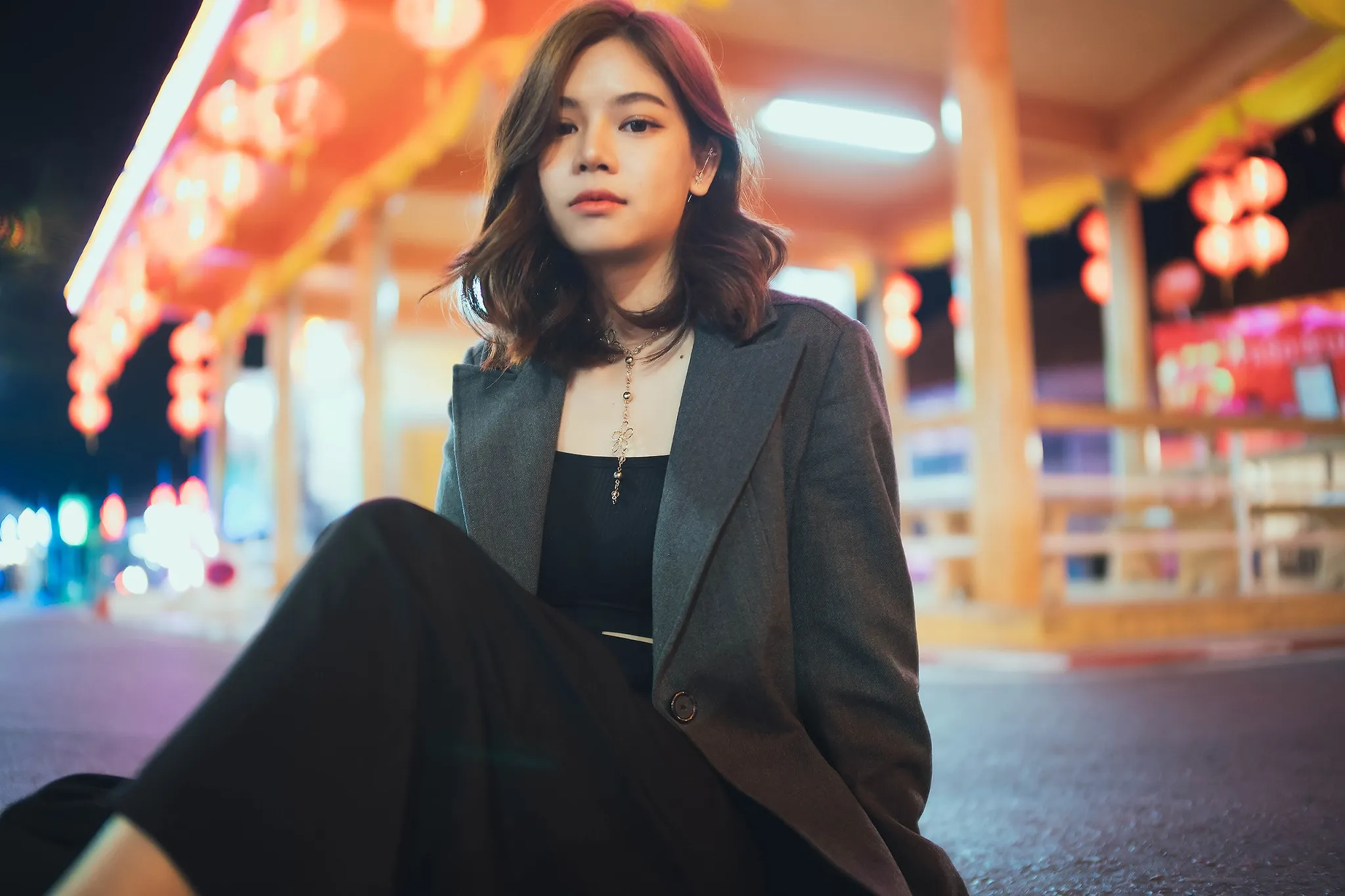 A woman in a grey blazer sitting on the ground in front of a lantern-lit pavilion at night