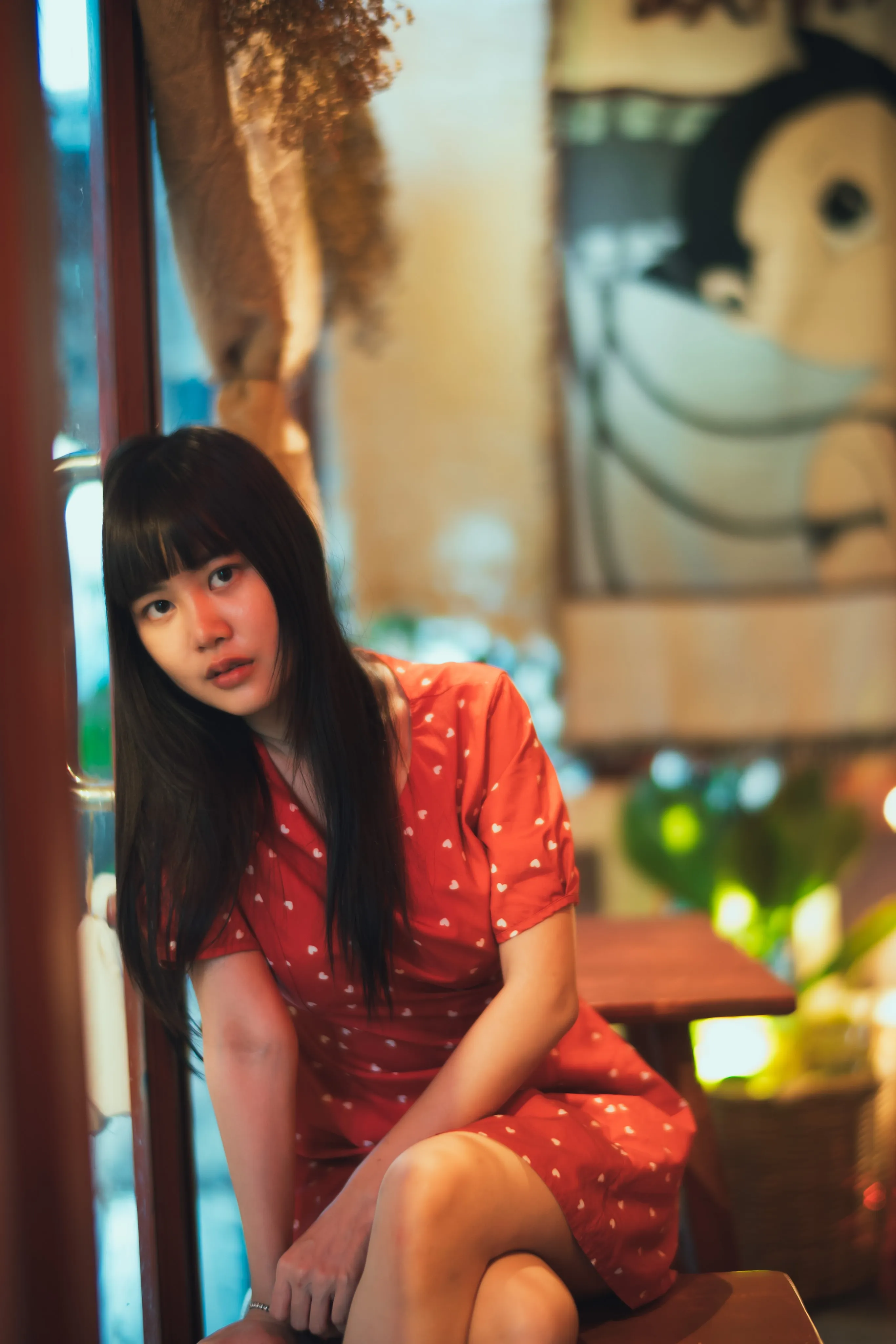 A woman in a red polka-dot dress sitting in a café beside a mural