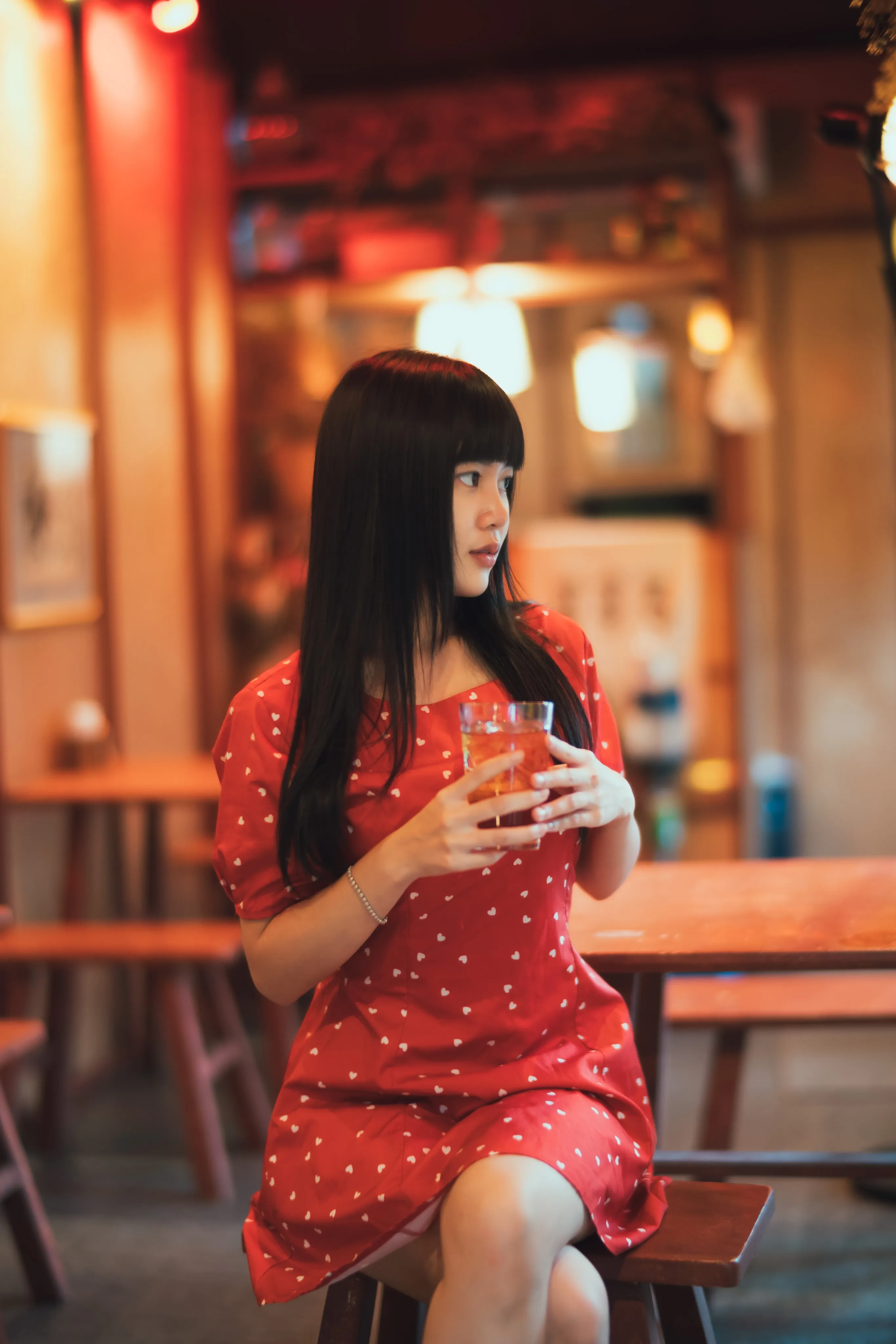 A woman in a red polka-dot dress holding a drink in a warmly lit café