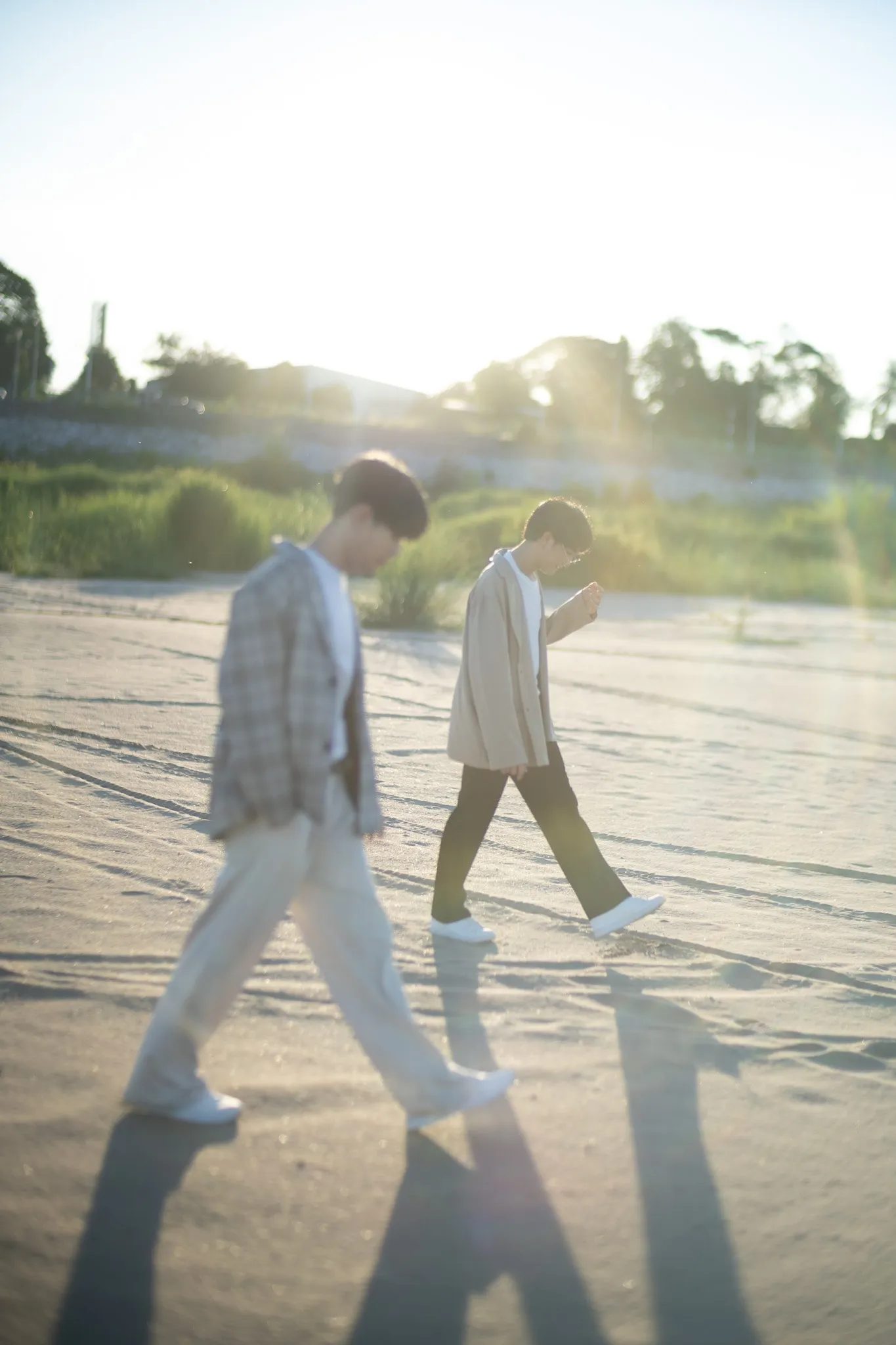 Two young men in blazers walking across sand with long shadows in low sunlight