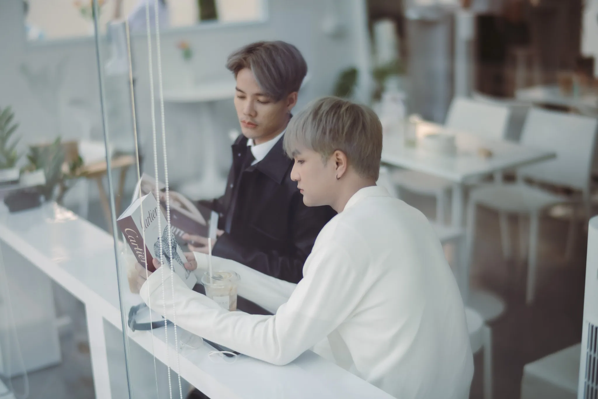 Two young men with dyed hair reading a magazine together at a white café counter