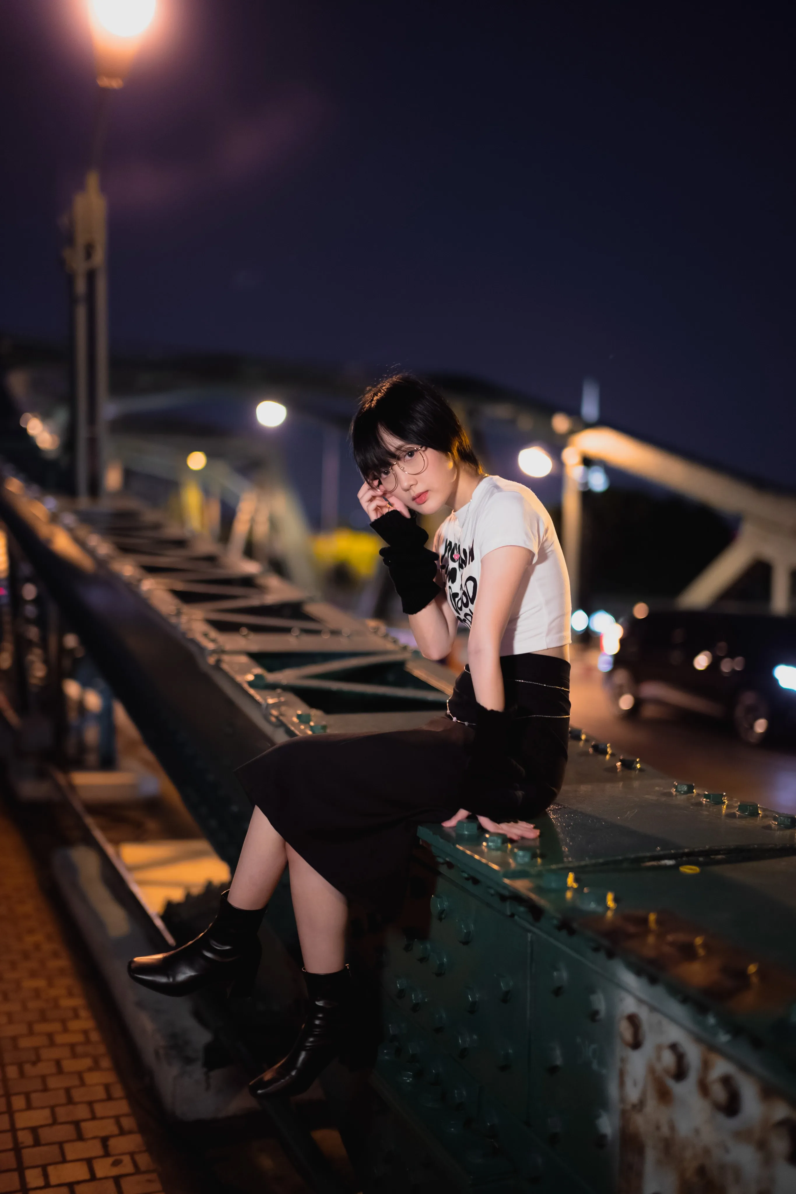 A woman sitting on a bridge railing above a city at night