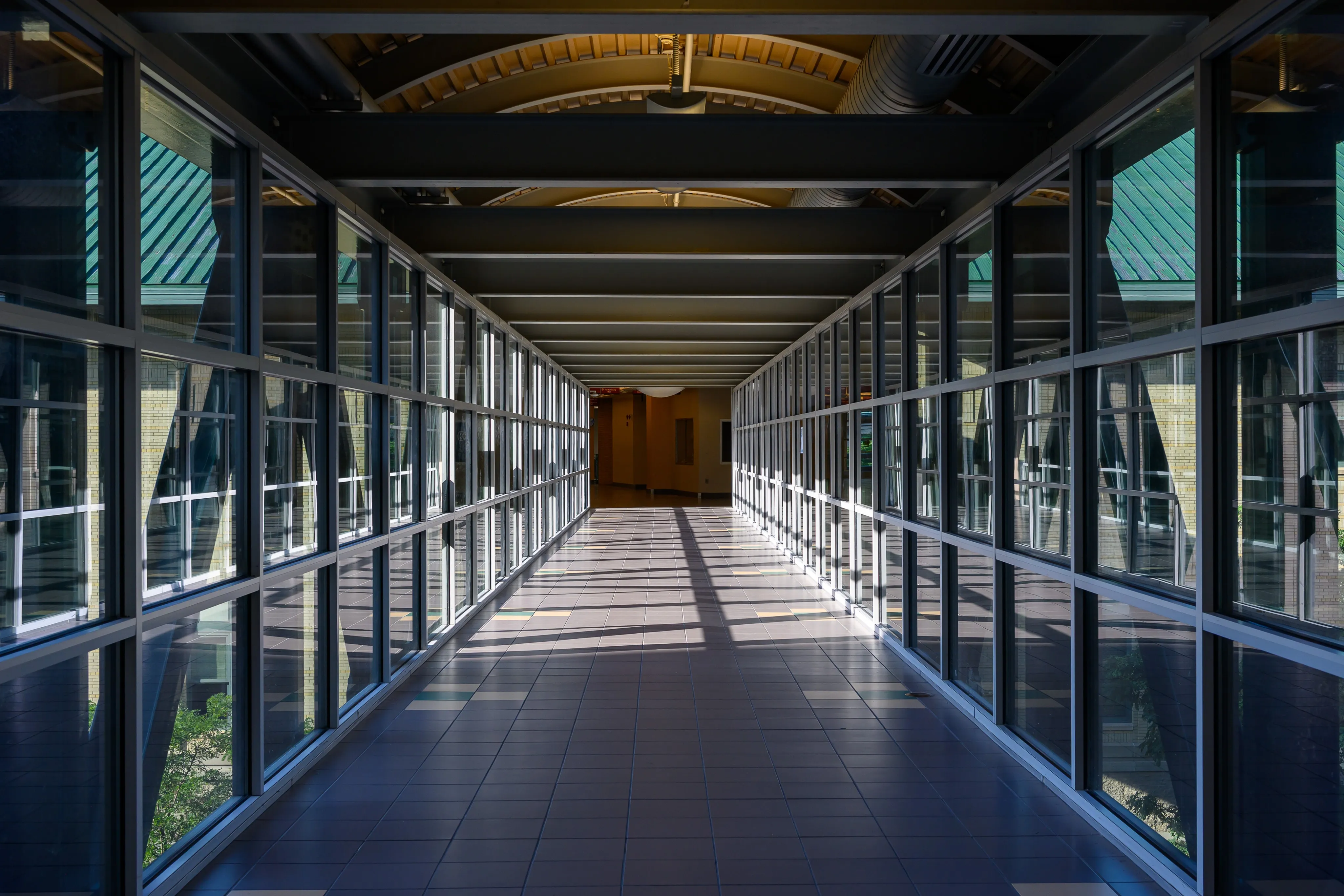 A long glass-walled skywalk corridor stretching into the distance, lit by afternoon sun.