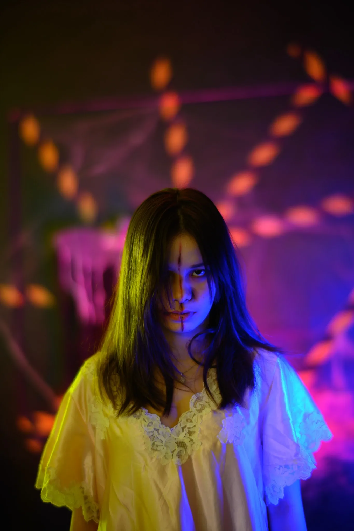 A woman in a yellow nightgown with long dark hair staring into the camera under eerie colored light