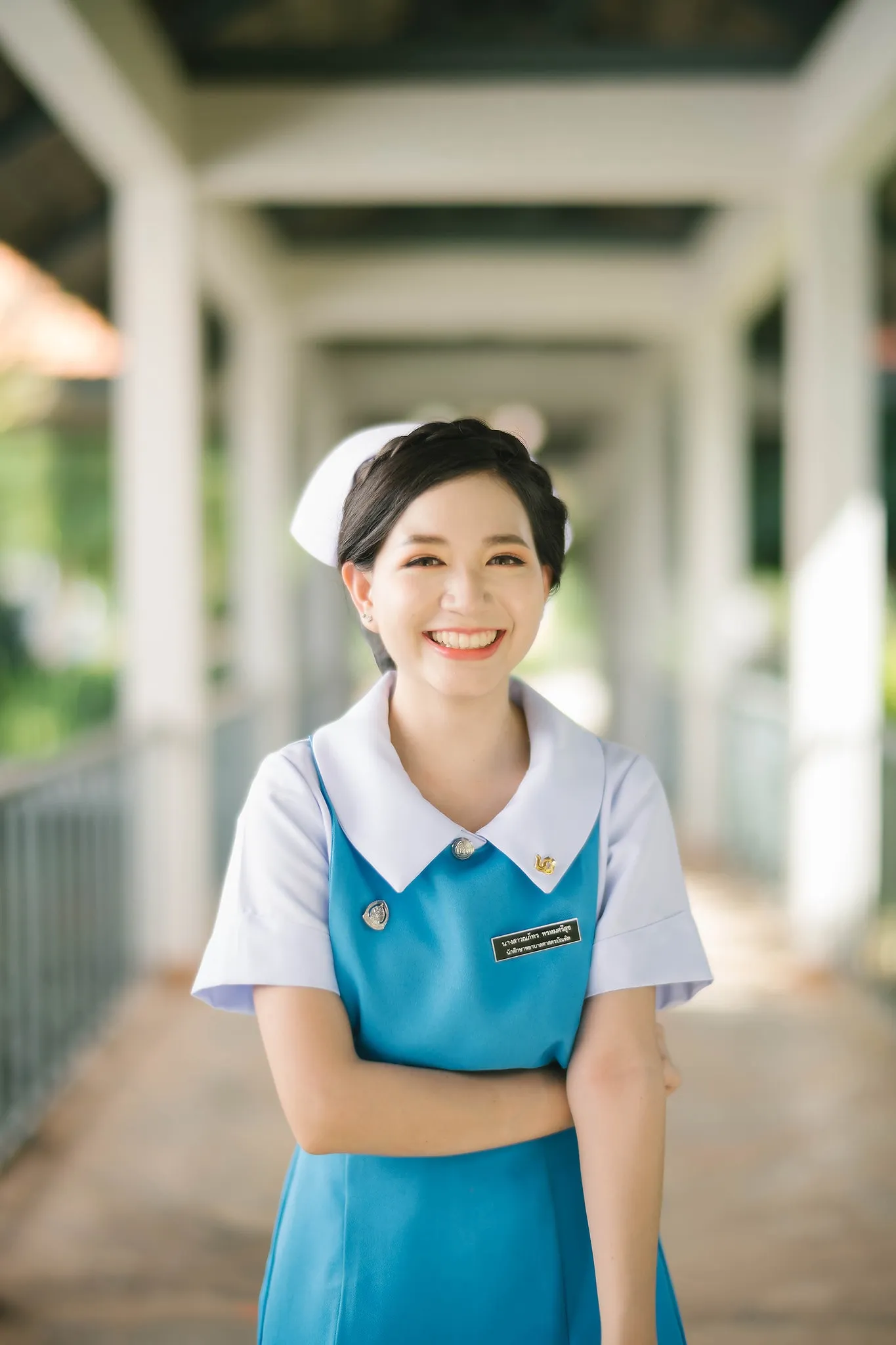 A graduate in a blue-and-white uniform smiling beneath a covered walkway