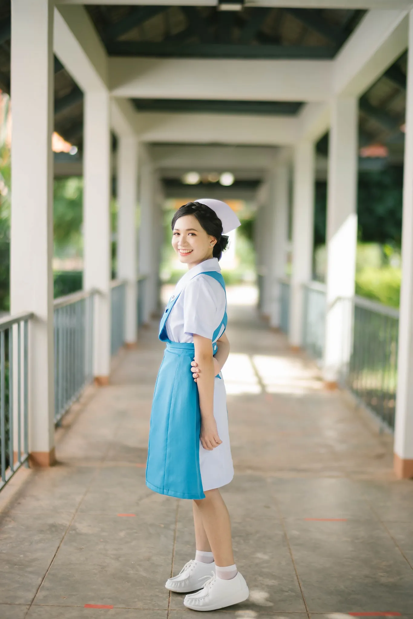 A graduate in a blue-and-white uniform standing along a covered walkway