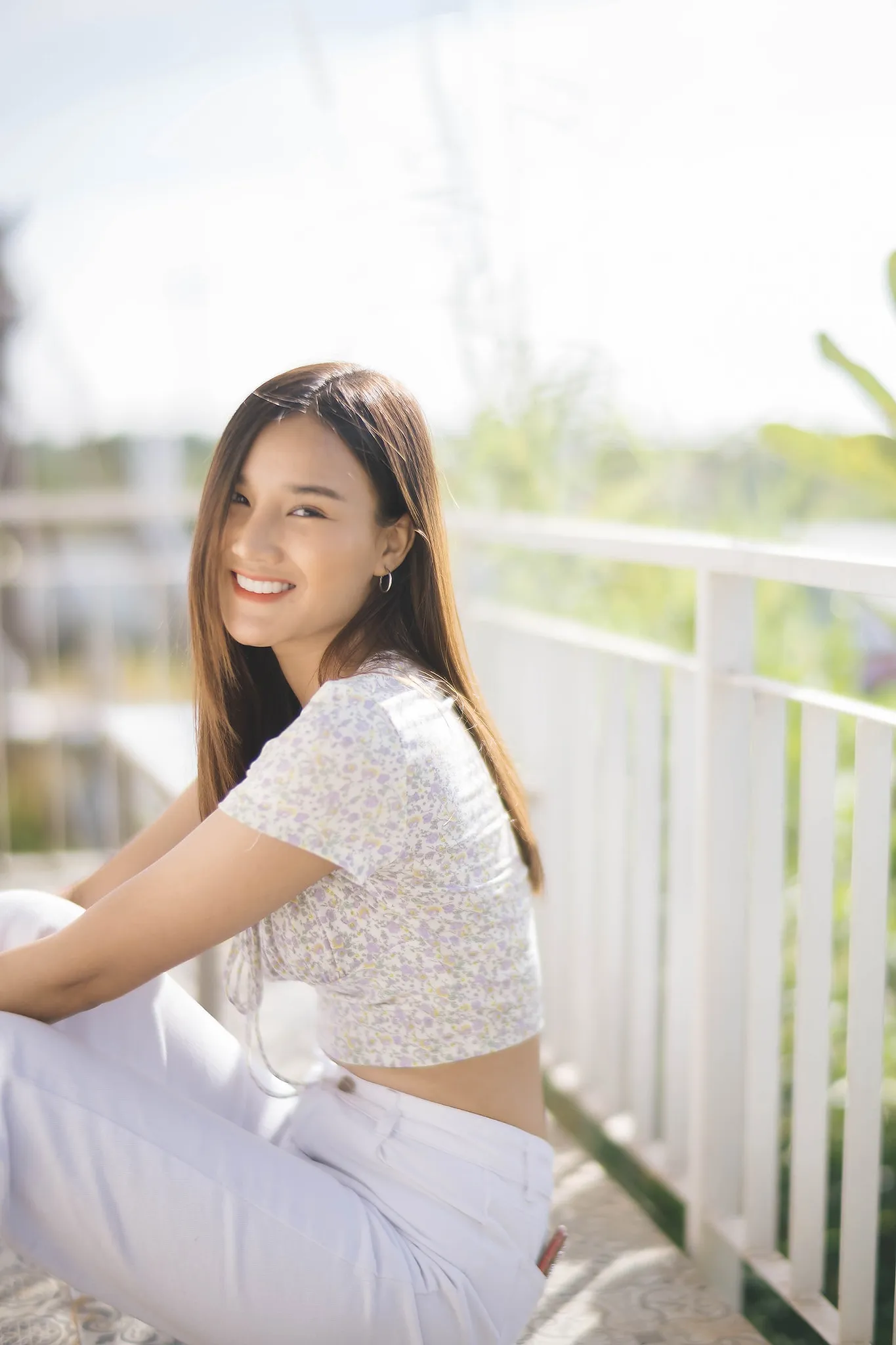 A smiling woman in white leaning against a sunlit railing