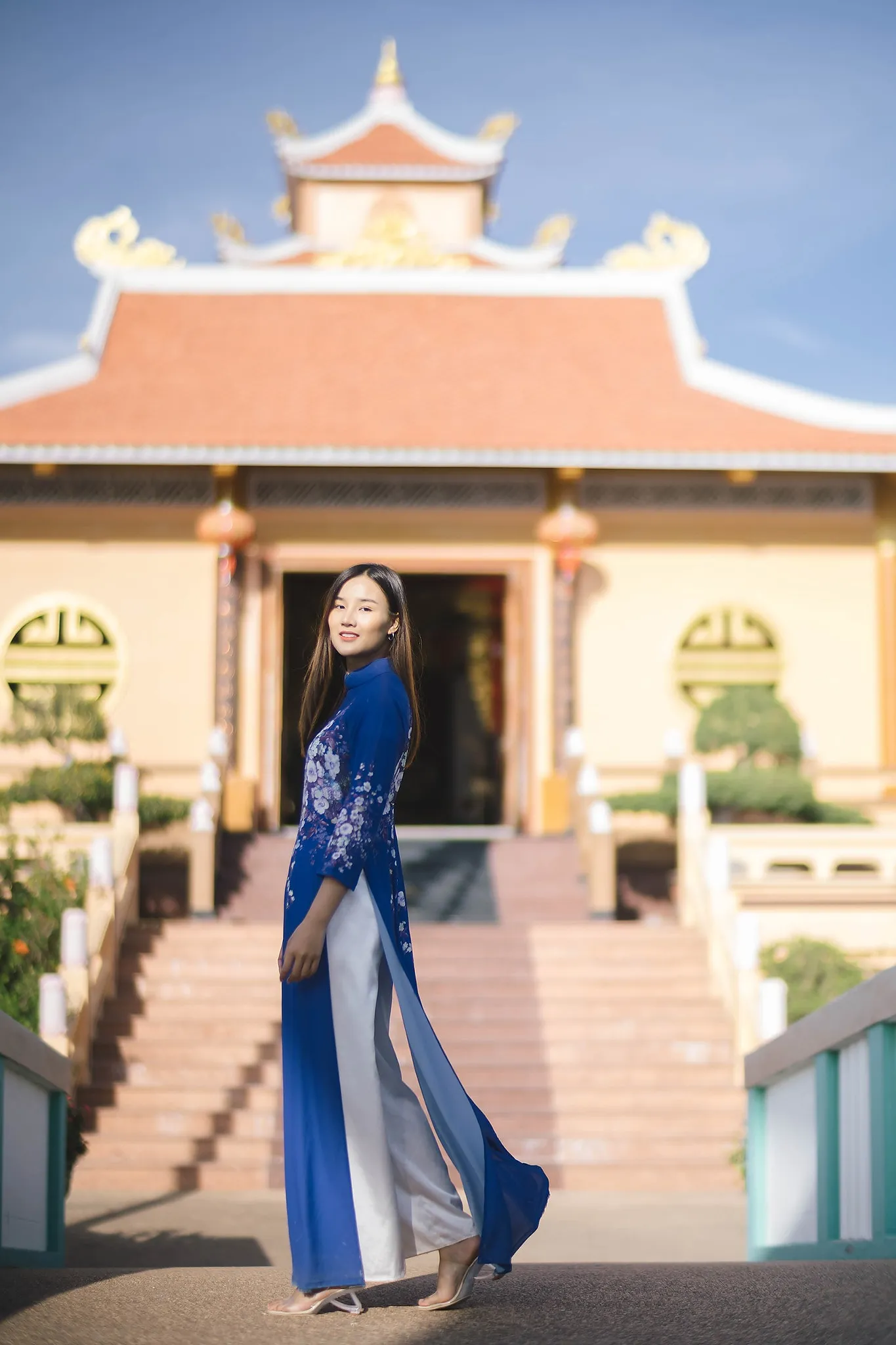 A woman in a blue ao dai posing before a traditional pavilion