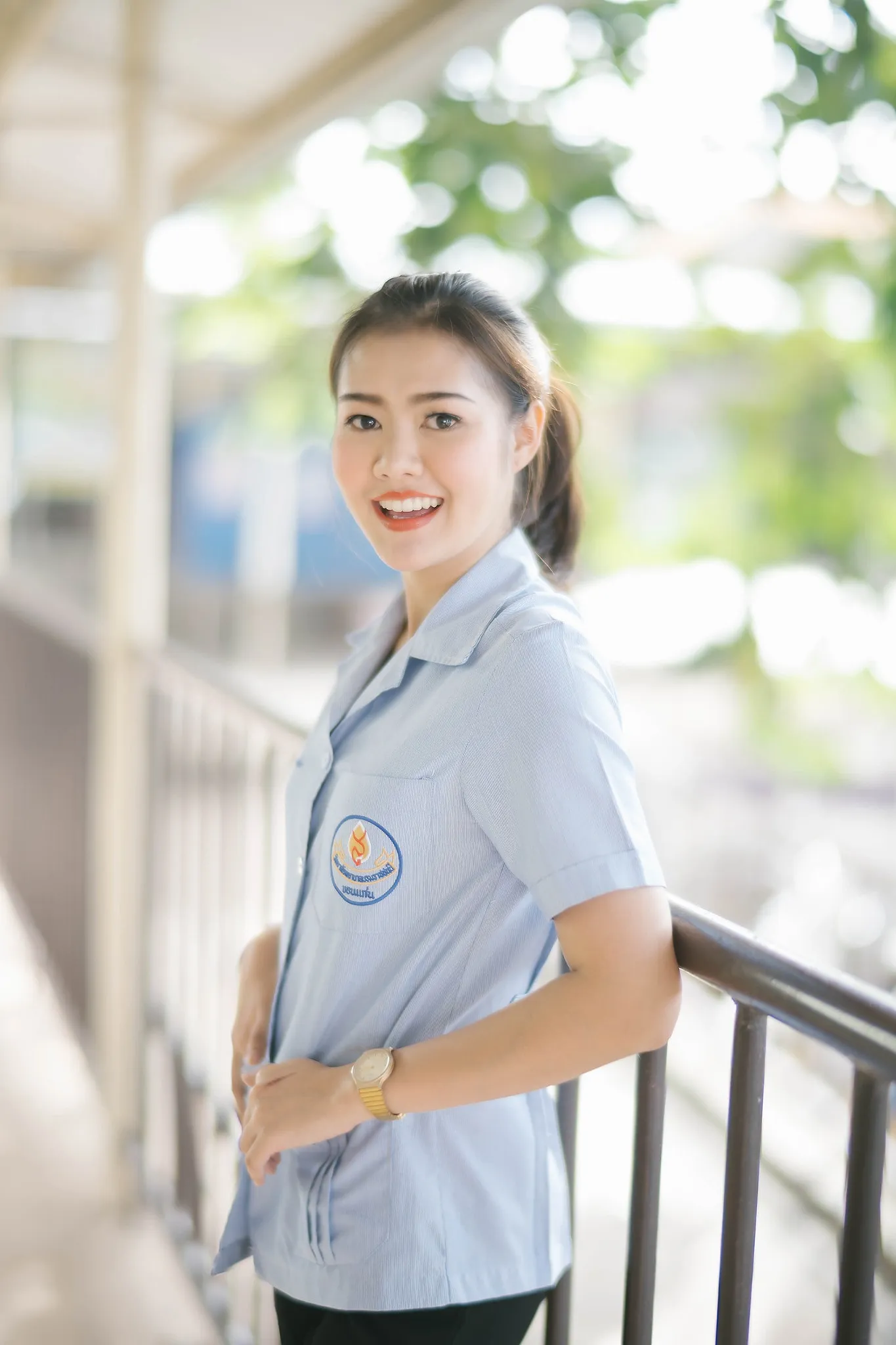 A student in a light blue uniform smiling on a balcony