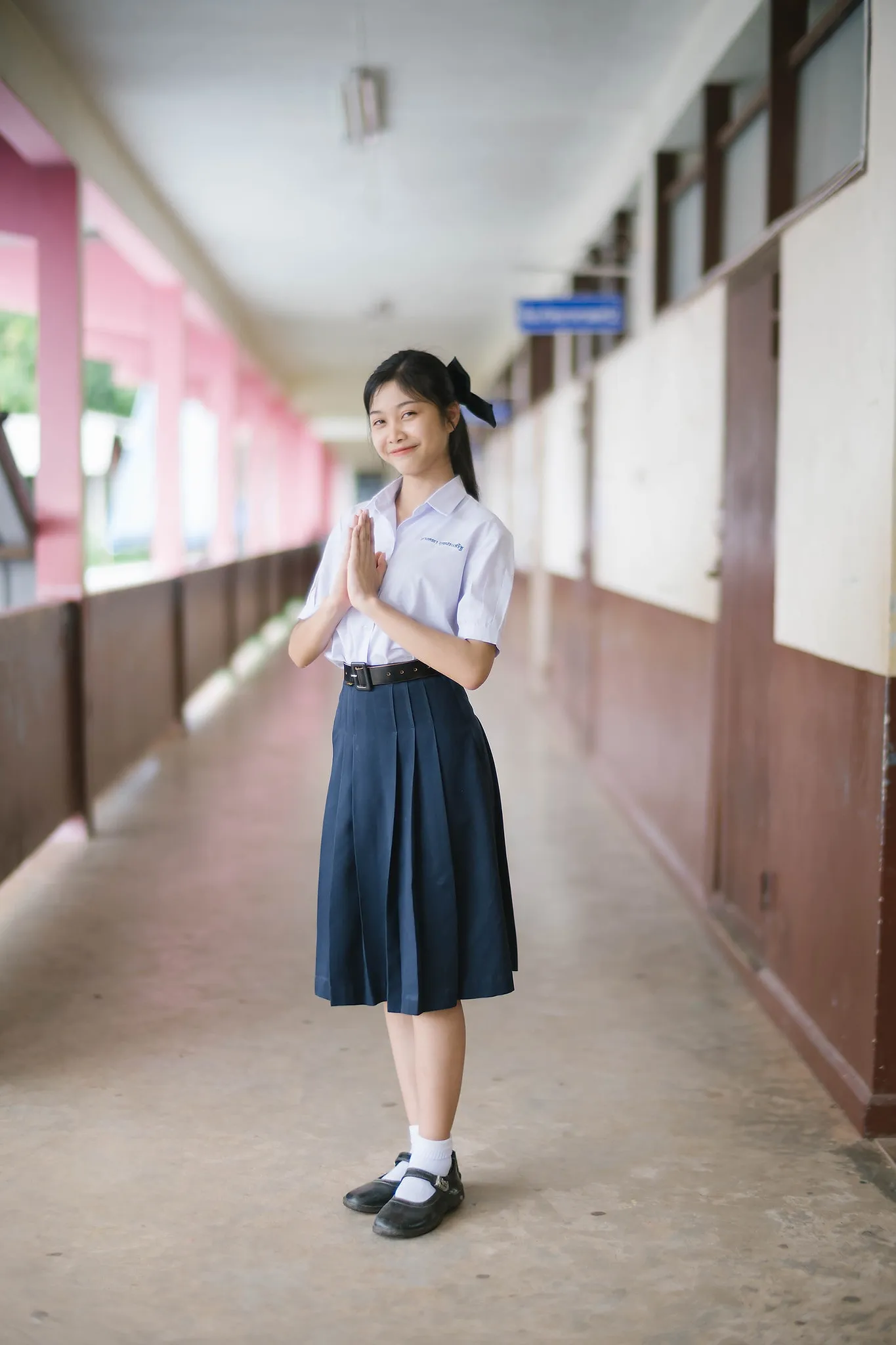 A student standing in a school corridor with hands clasped