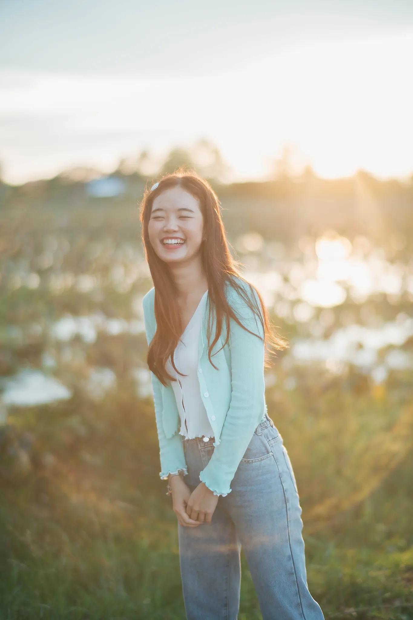 A woman smiling in golden backlight near a green field