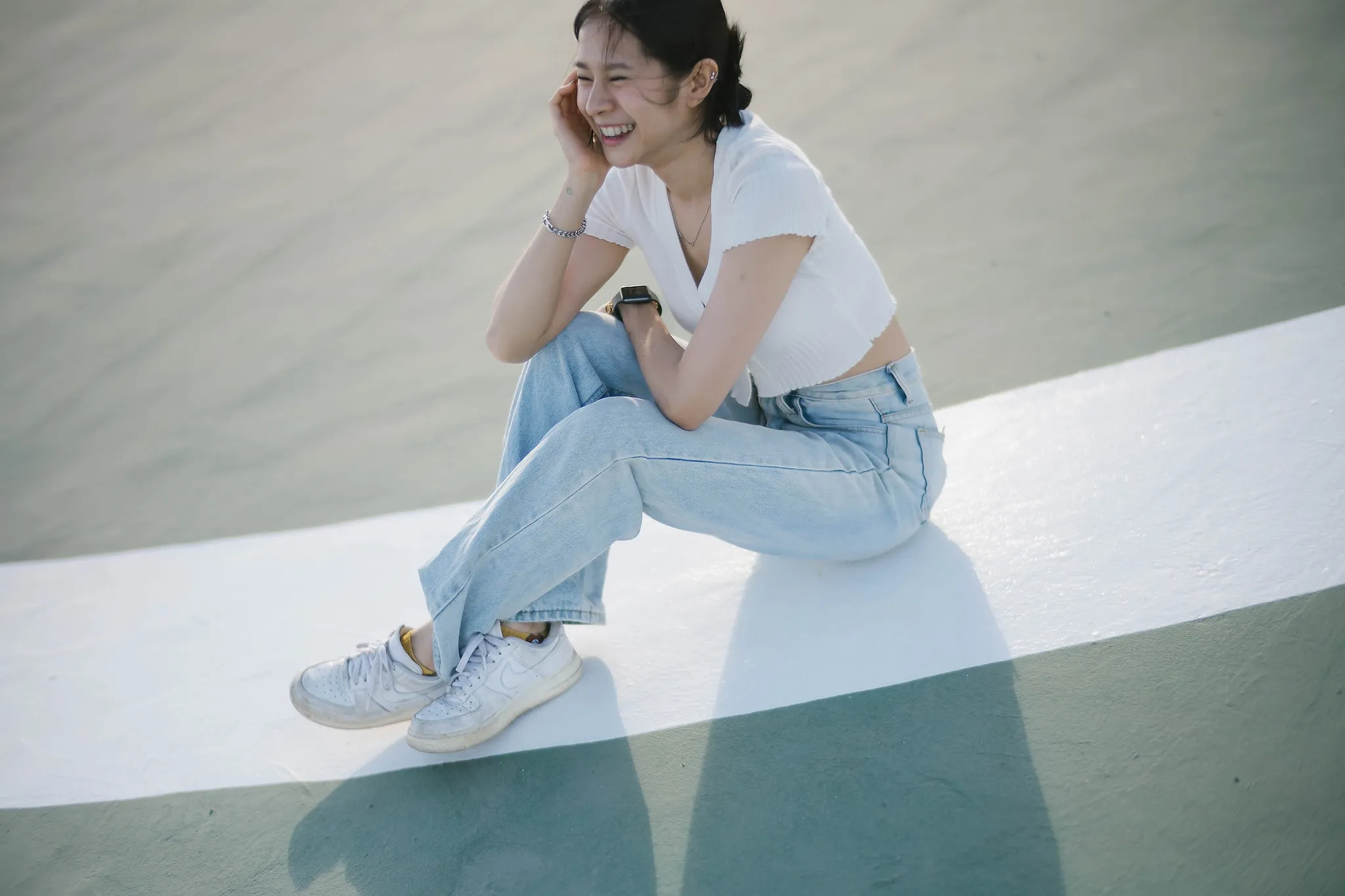 A woman seated on a concrete ledge in bright sunlight
