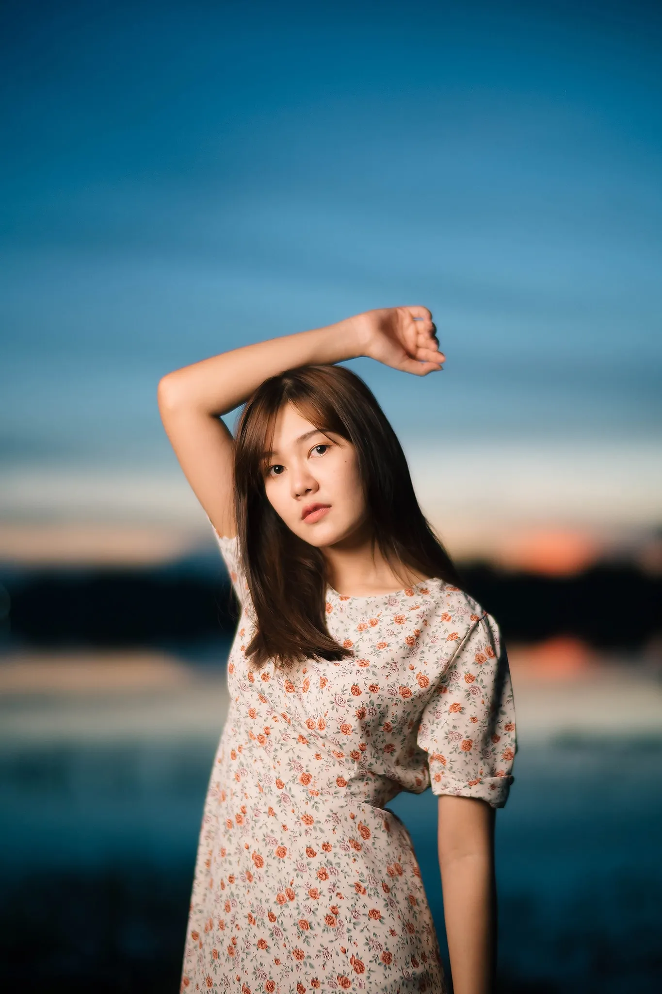 A woman in a floral dress posing against a deep blue evening sky