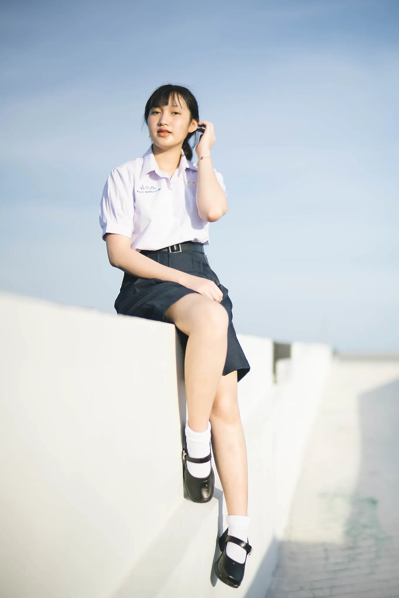 A student in uniform seated on a white wall beneath a blue sky