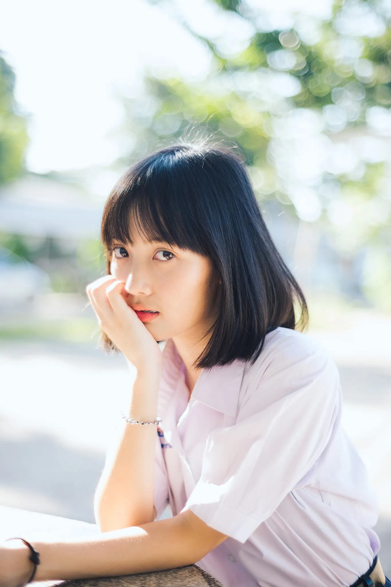 A student in a white blouse resting her chin on her hand outdoors