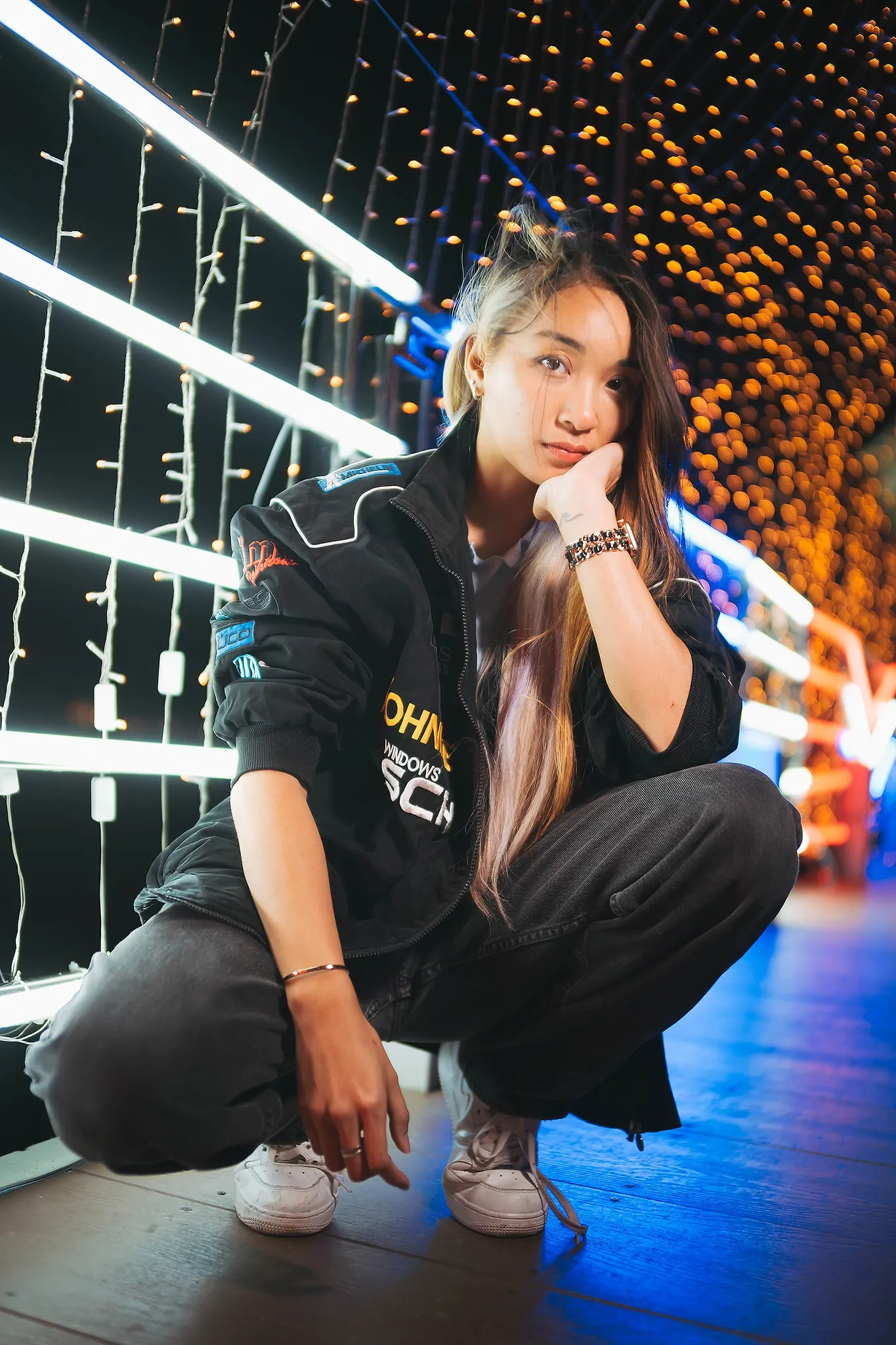 A performer in black streetwear crouching beneath colorful lights