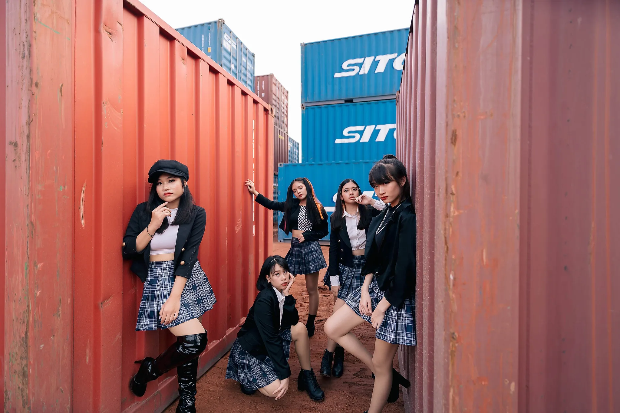 A group in coordinated black outfits posing between red shipping containers