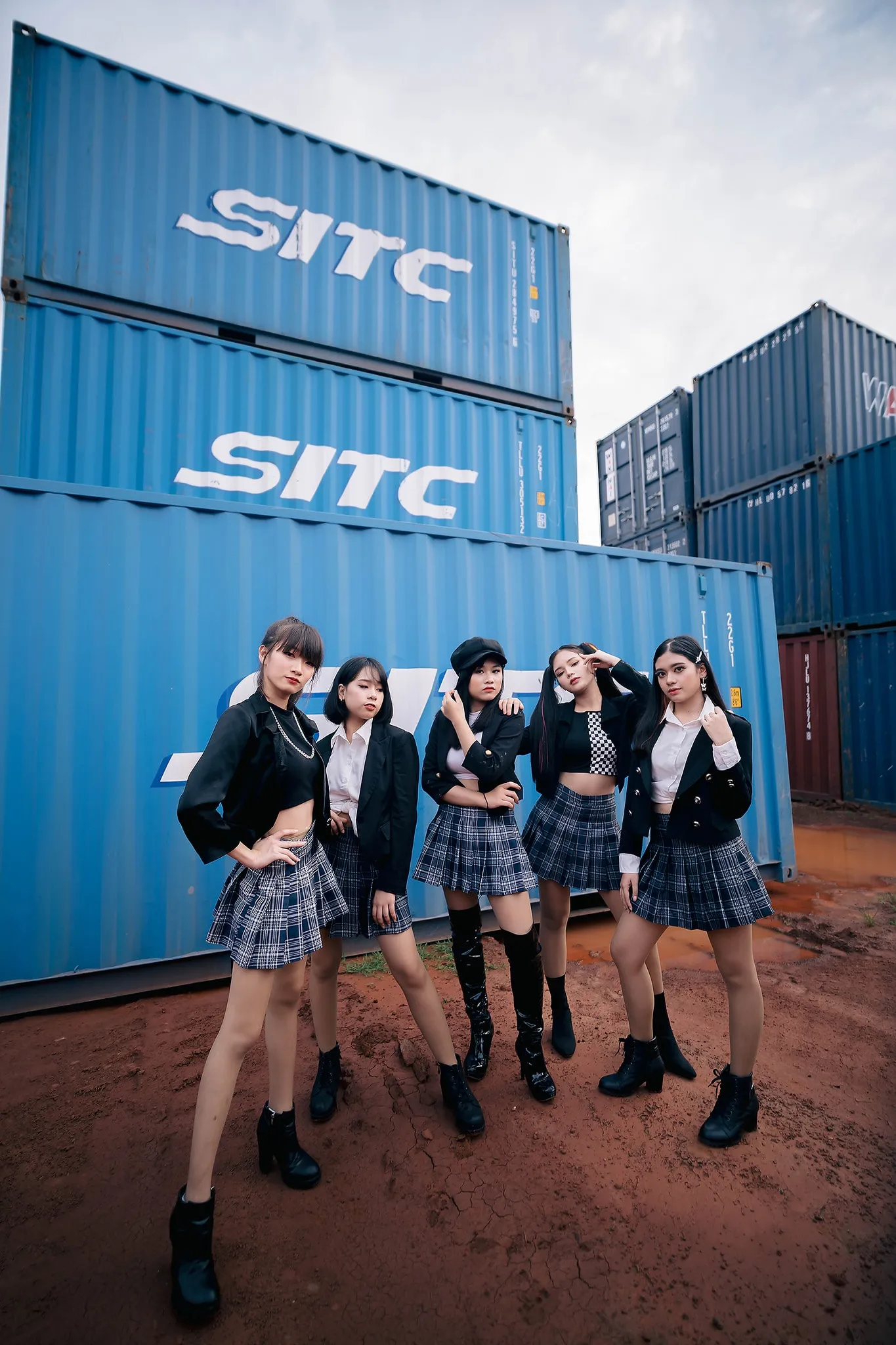 A group in coordinated black outfits posing before stacked shipping containers