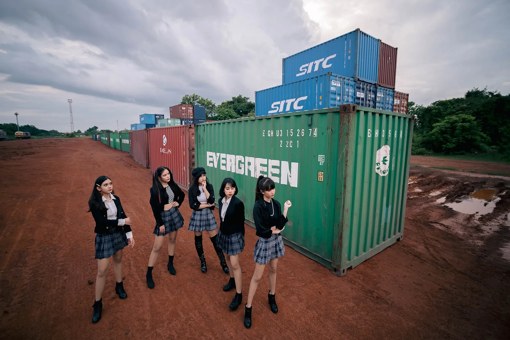 Five performers in black outfits standing among colorful shipping containers