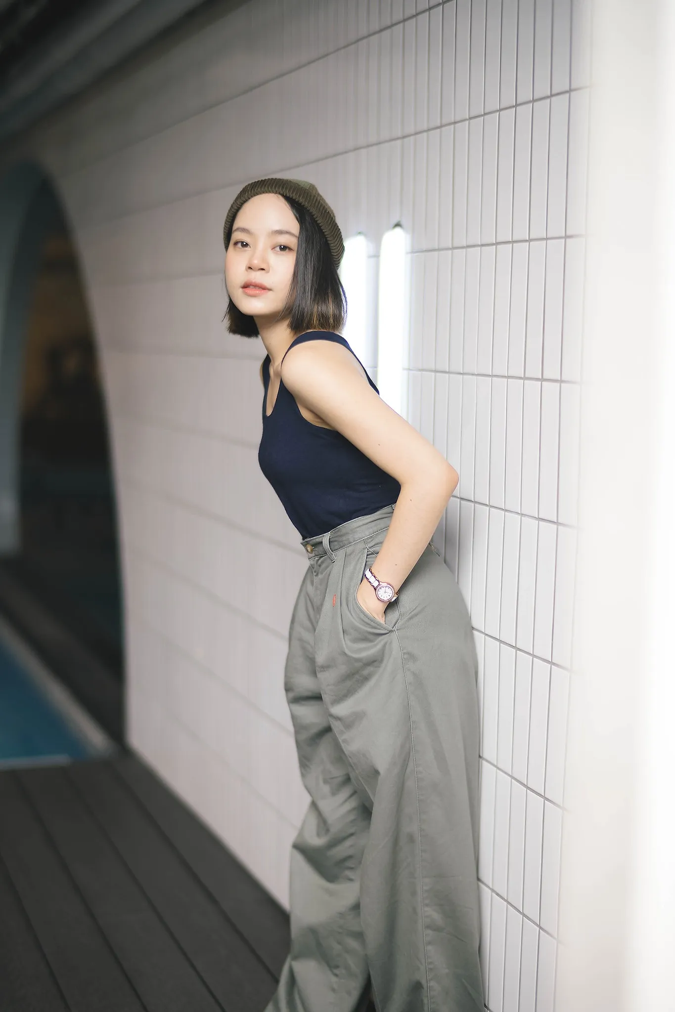 A woman in a black sleeveless top posing beside a tiled wall