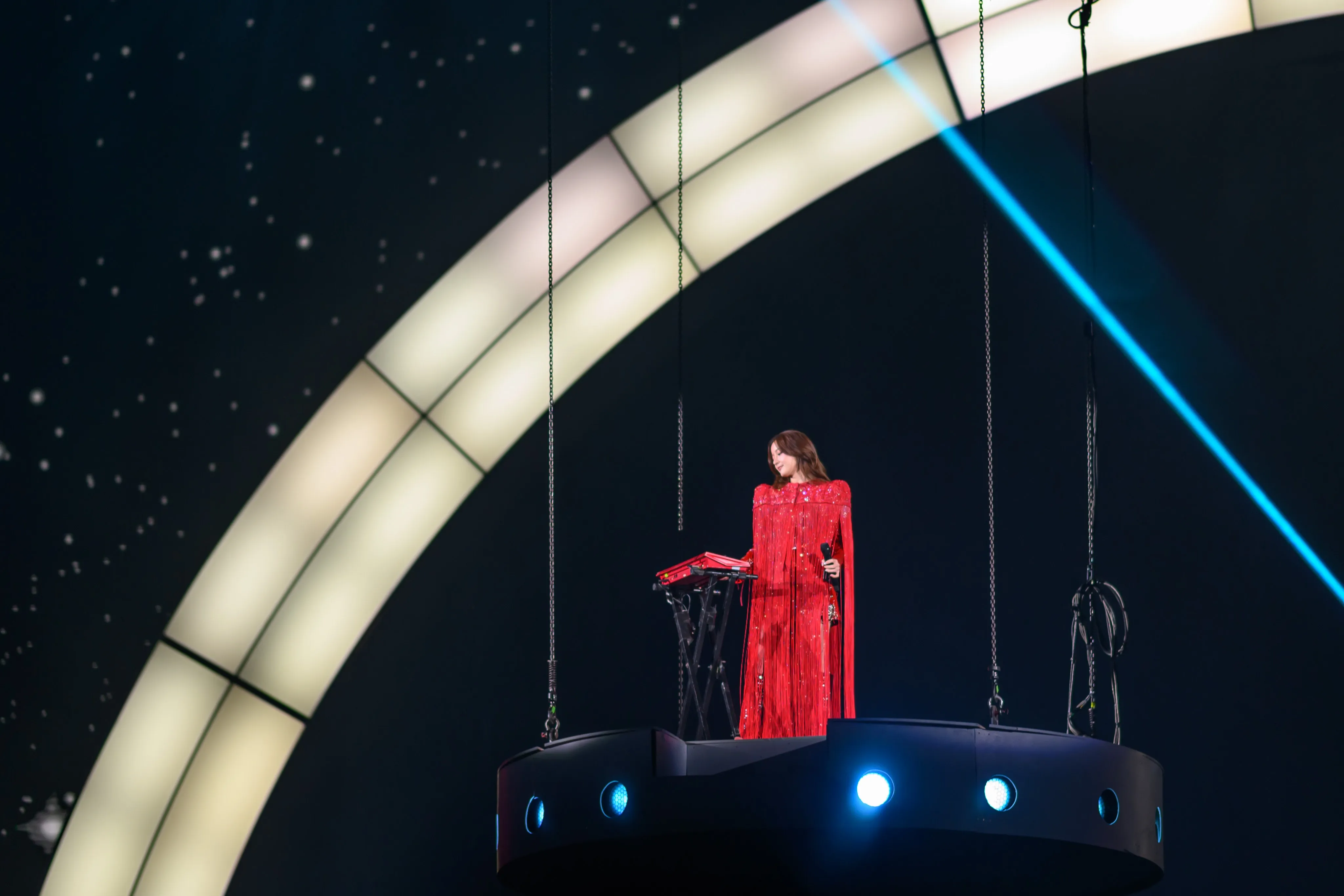 A performer singing on stage under an arched light structure