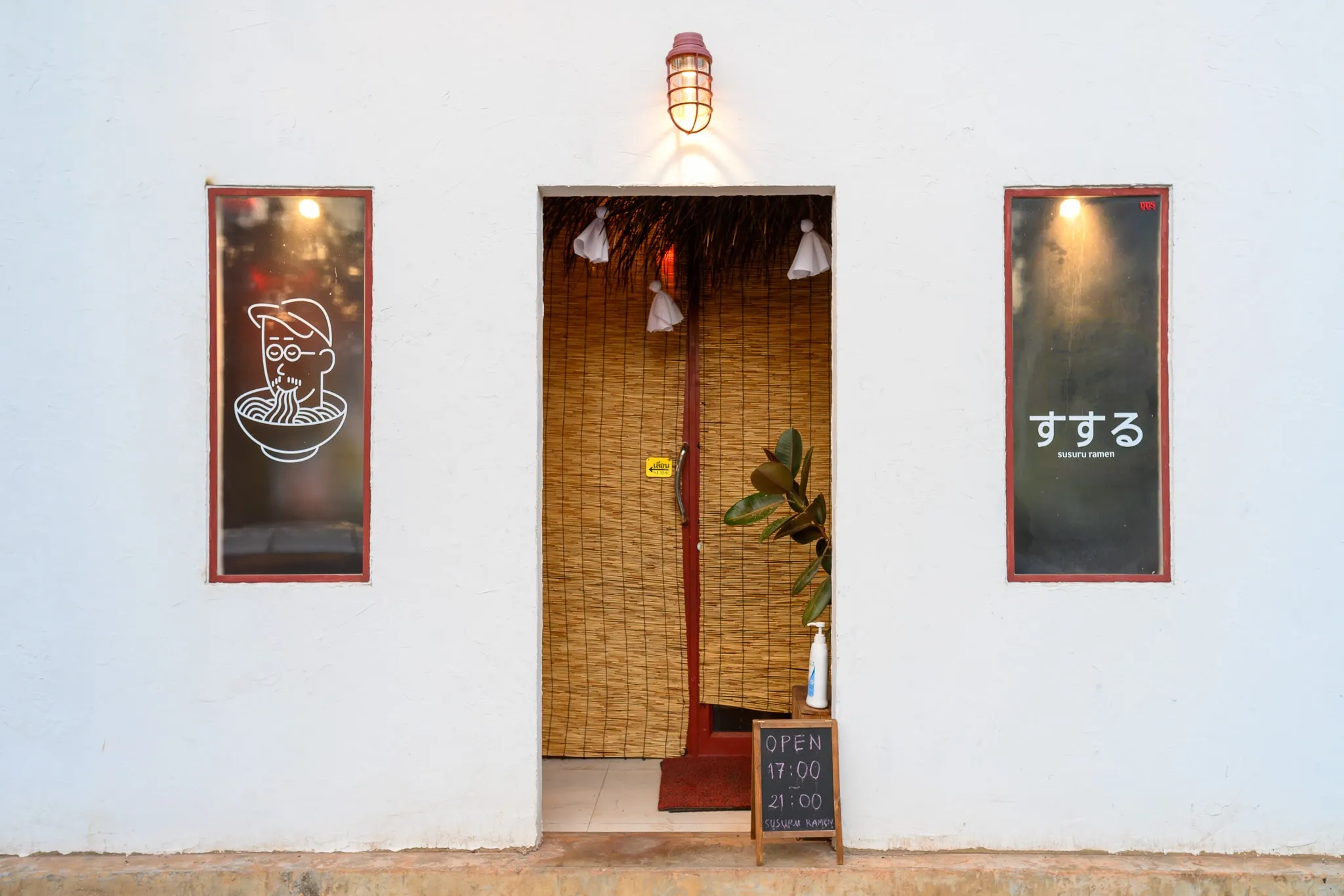 A white ramen shop front with a bamboo curtain doorway and illustrated window panels
