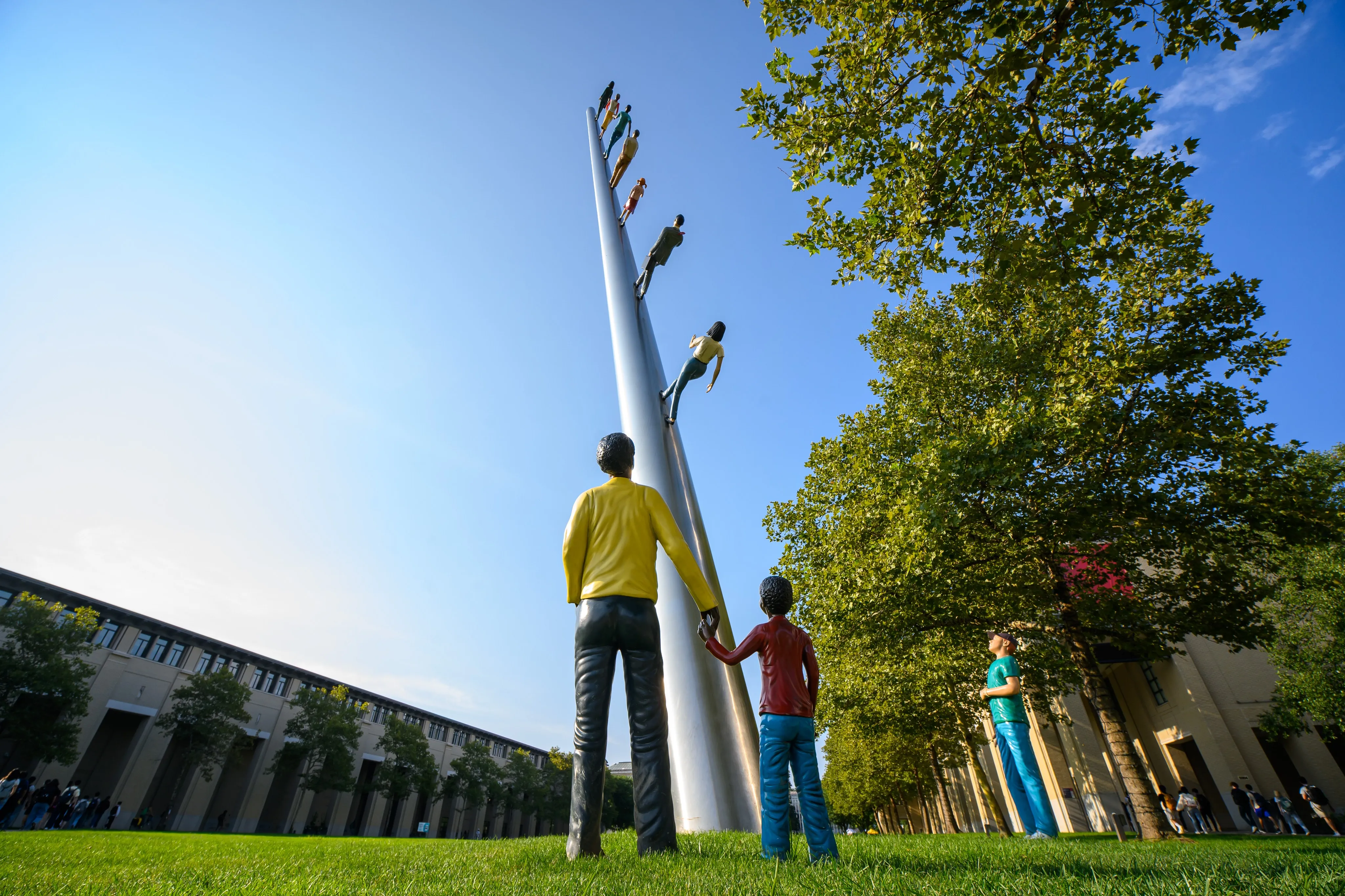 Jonathan Borofsky's "Walking to the Sky" sculpture rising above a row of pine trees against a blue sky.