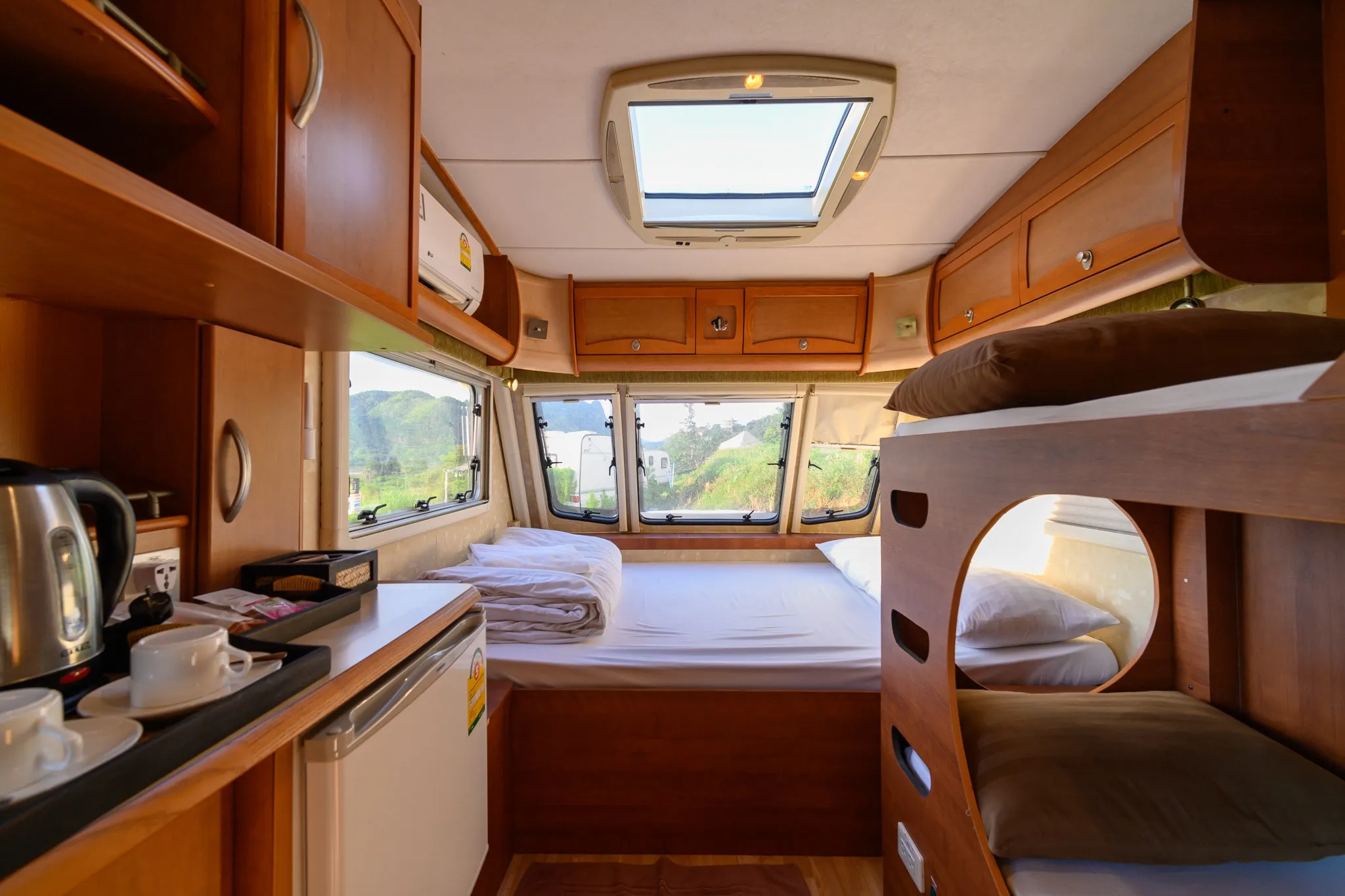 The wood-paneled interior of a camper van with a bed, bunk, and kitchenette