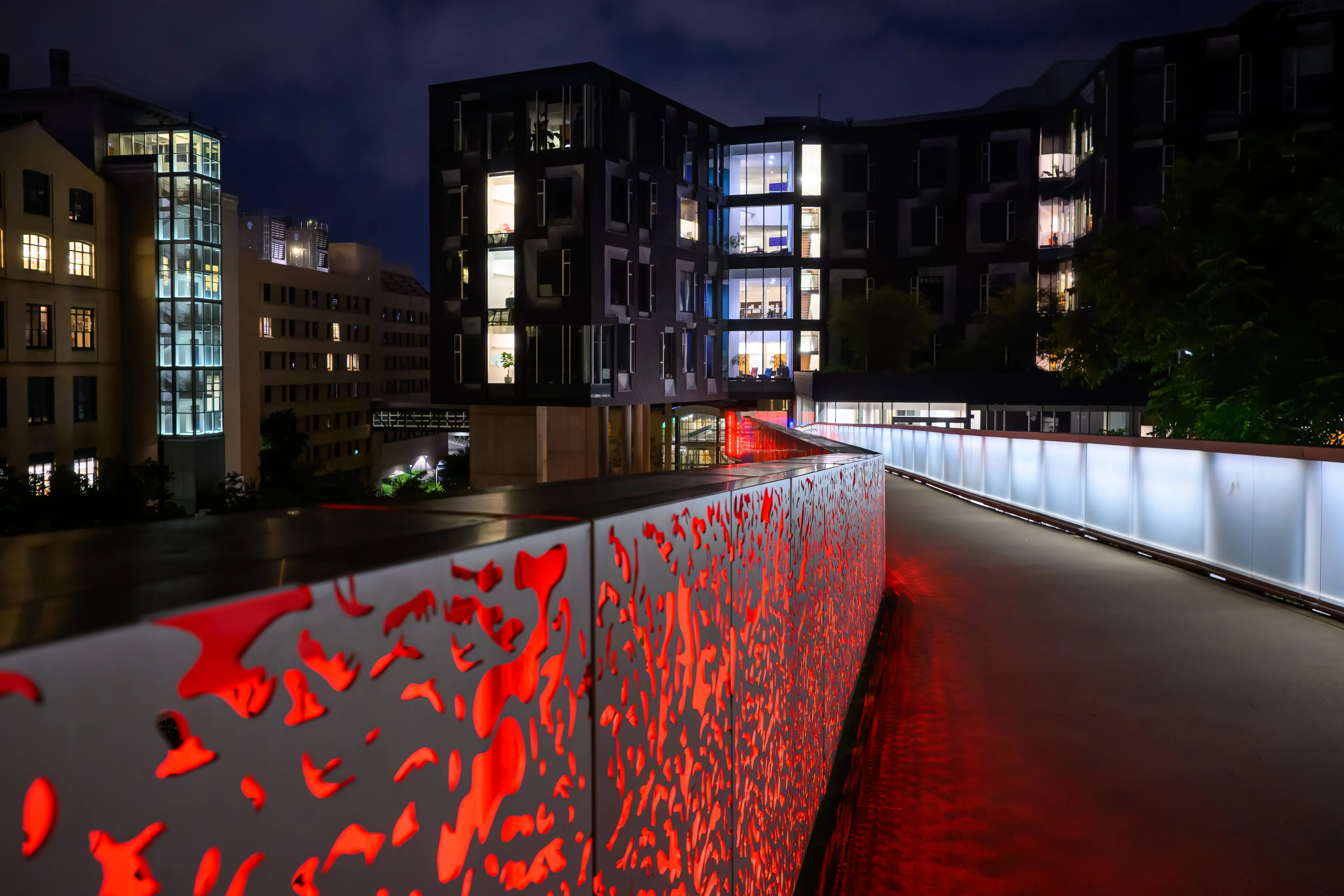 A modern skywalk glowing red at night between two campus buildings.