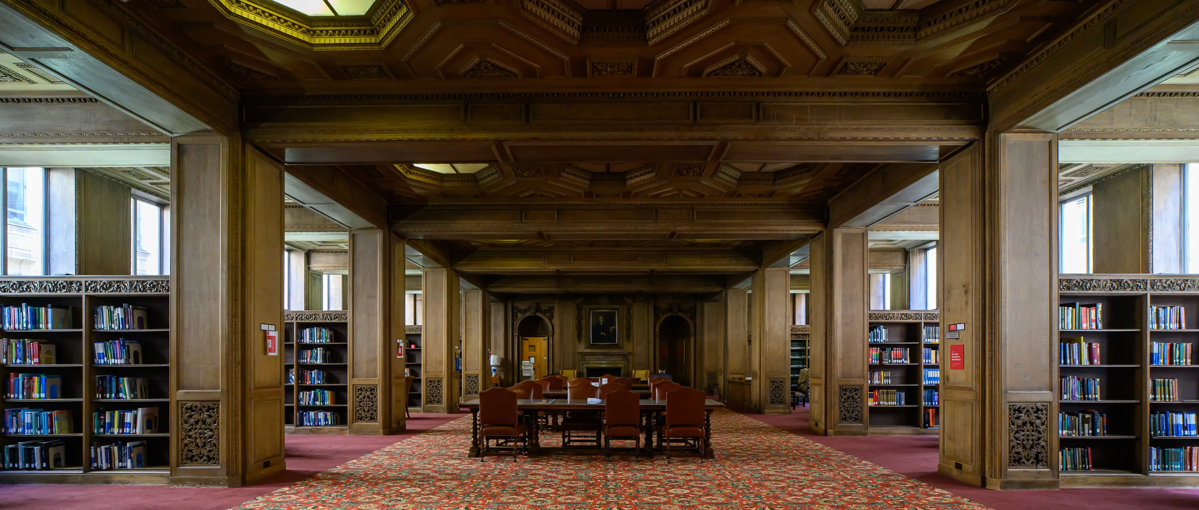 Rows of bookshelves and reading tables in a warmly lit library interior.