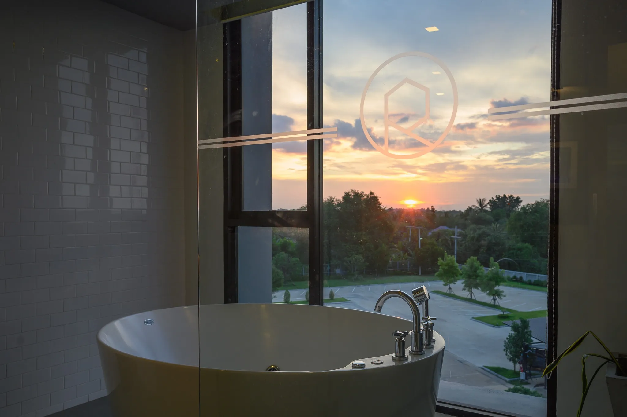 A round bathtub at a window overlooking trees at sunset