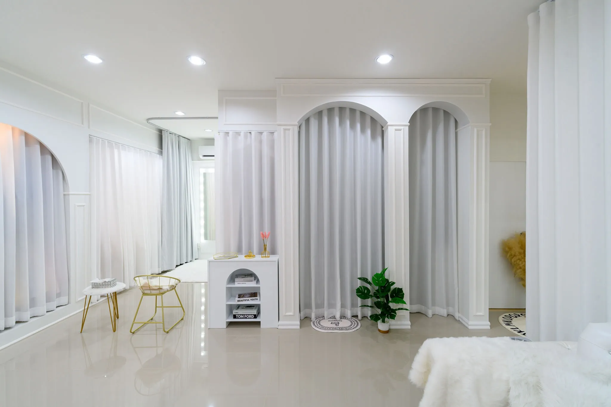 Arched white fitting-room curtains and gold chairs in a minimalist bridal studio