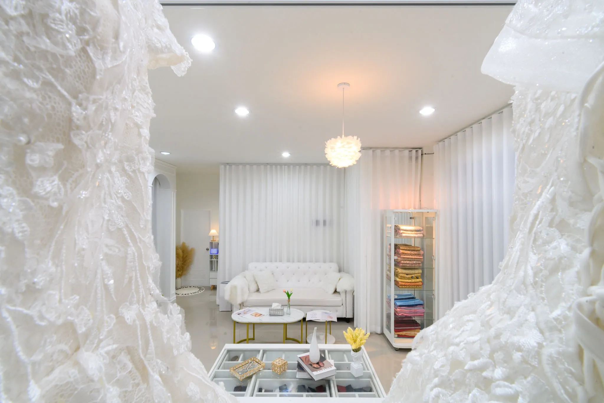 A bright white lounge with a tufted sofa, seen between the lace folds of a wedding gown