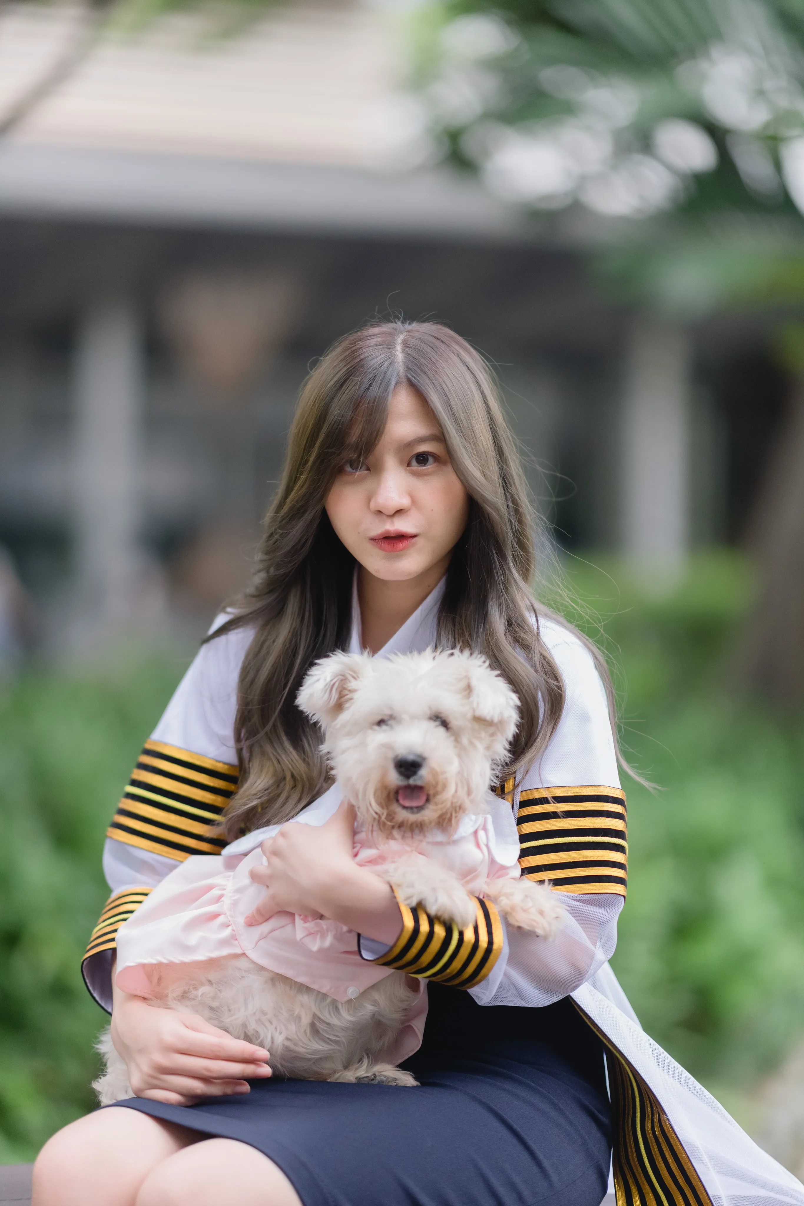 A graduate in a striped academic gown holding a small white dog dressed in pink