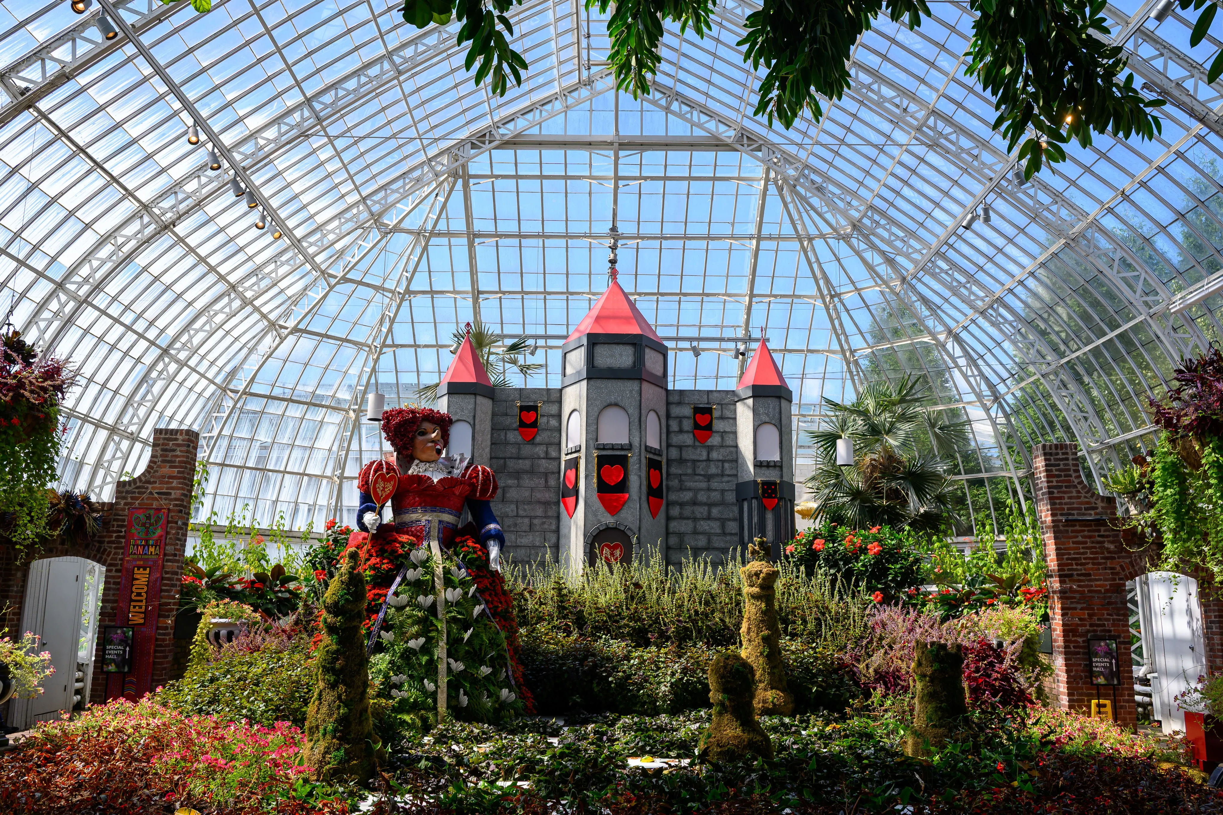 A castle-themed floral display beneath the glass dome of a botanical conservatory.
