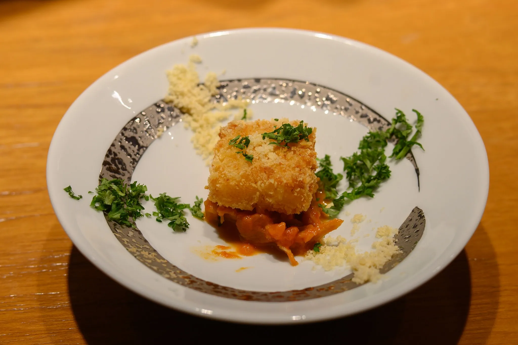A breaded croquette on tomato sauce with parsley and grated cheese in a silver-rimmed bowl