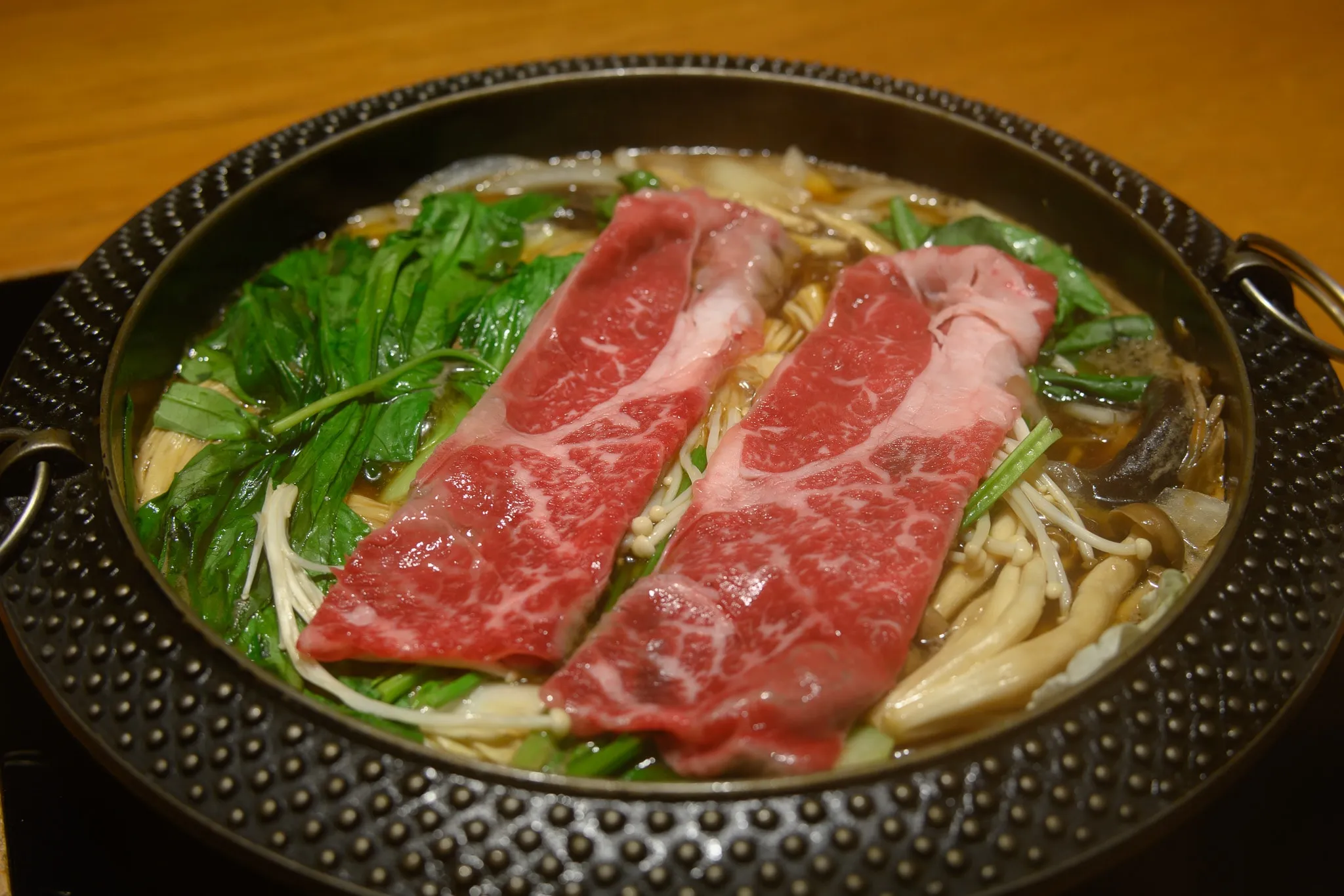 Marbled beef slices over mushrooms and greens in a black sukiyaki pot
